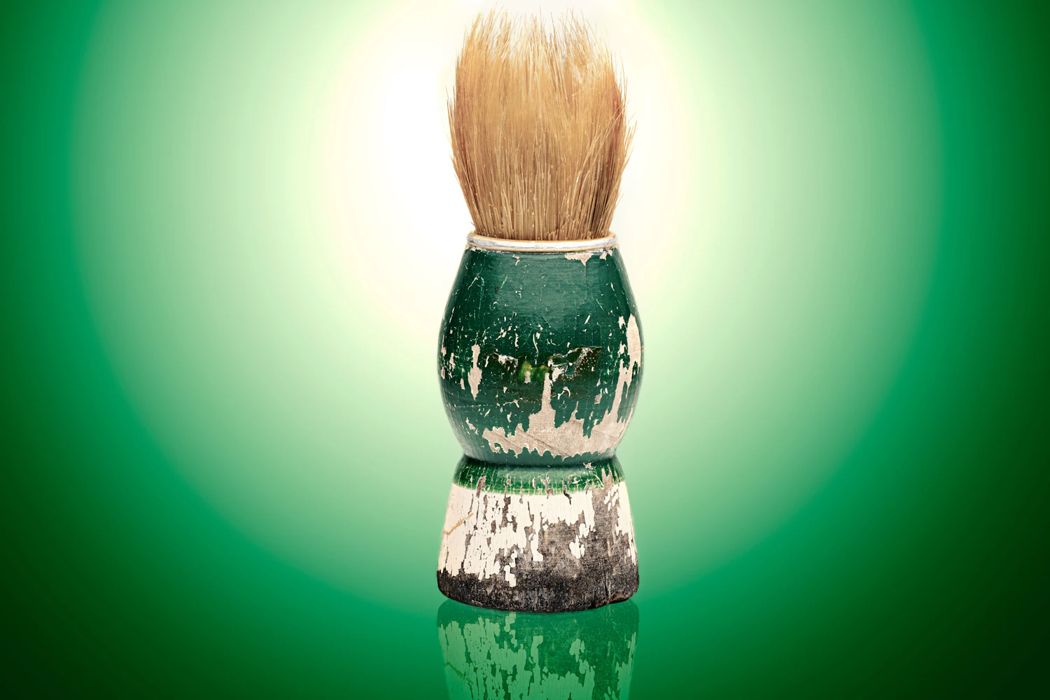 A worn shaving brush with a chipped handle standing on a green ground
