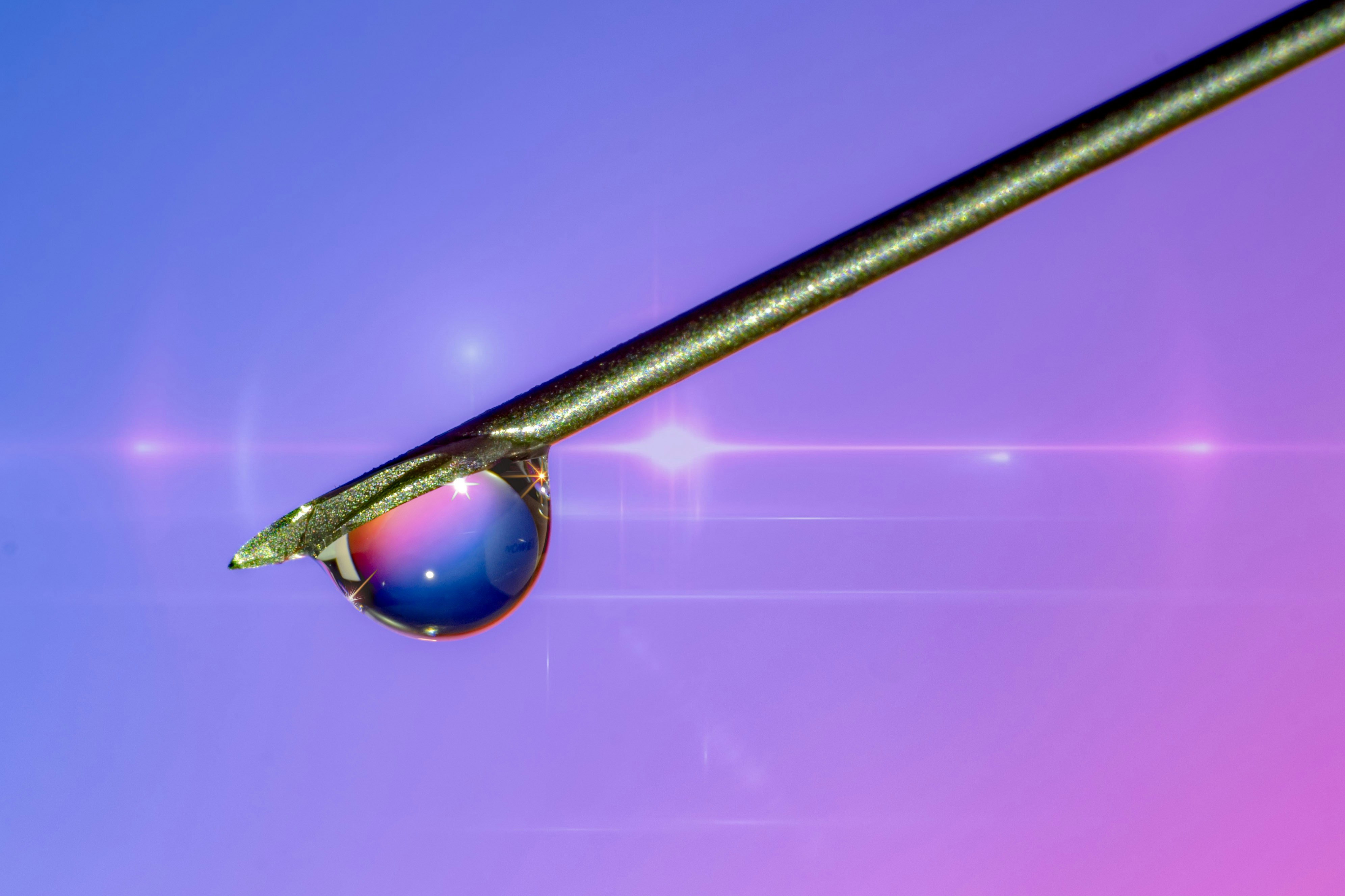 Needle tip holding a liquid drop reflecting colorful light