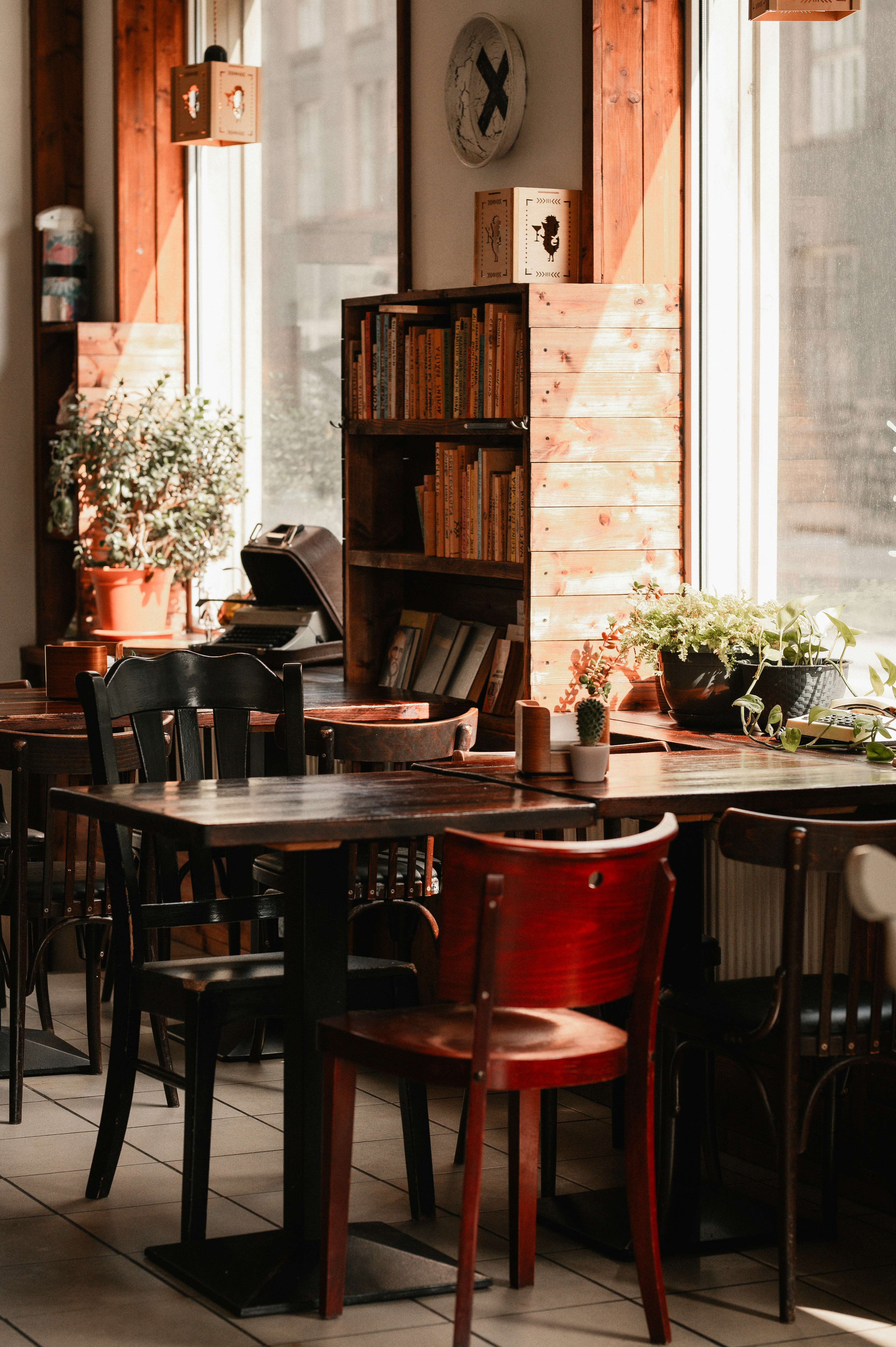 Cozy cafe interior with tables, chairs, books, and sunlight.