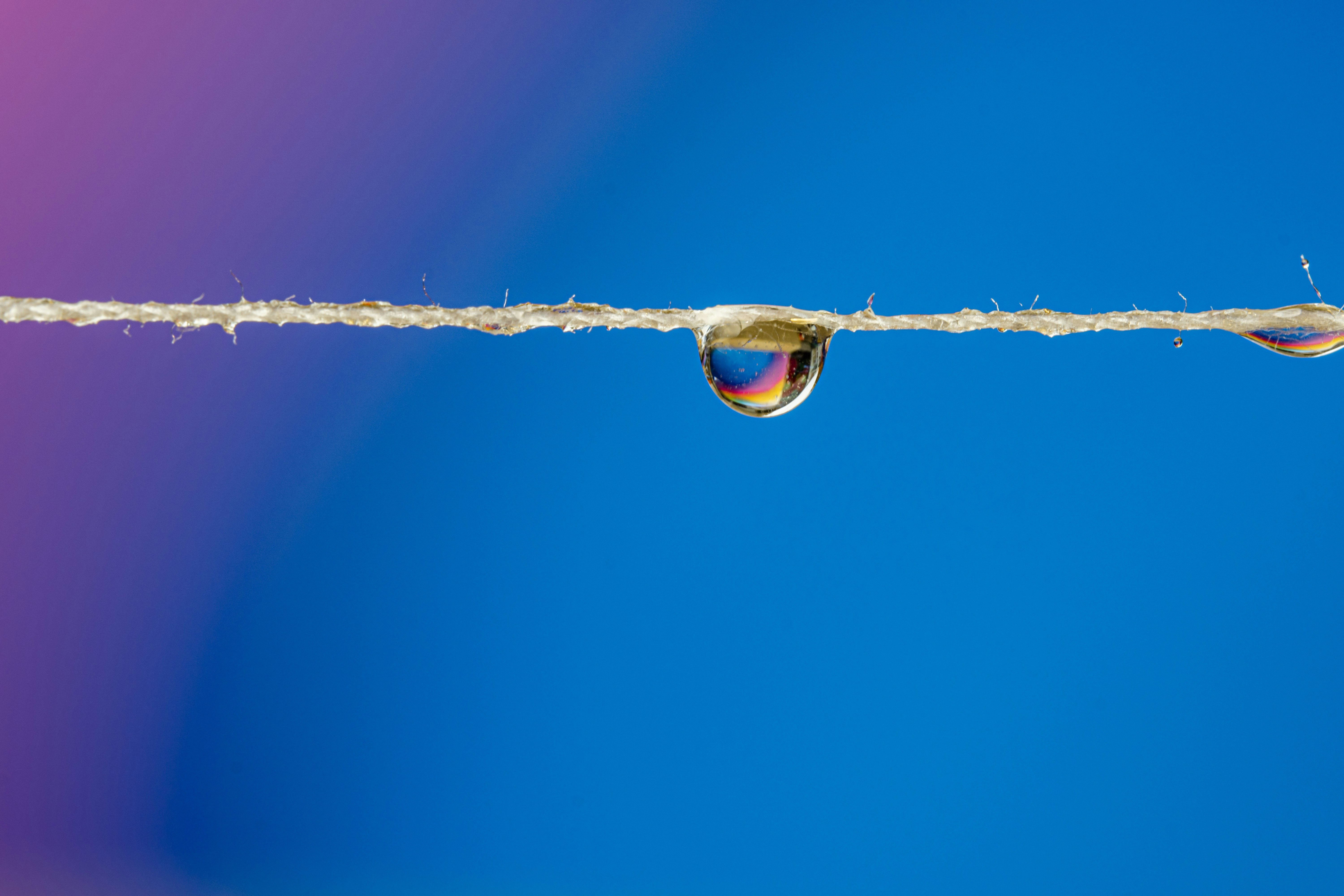 Colorful water droplet suspended from a string against blue background