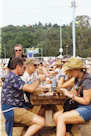 Friends at picnic benches with drinks, toilets sign.