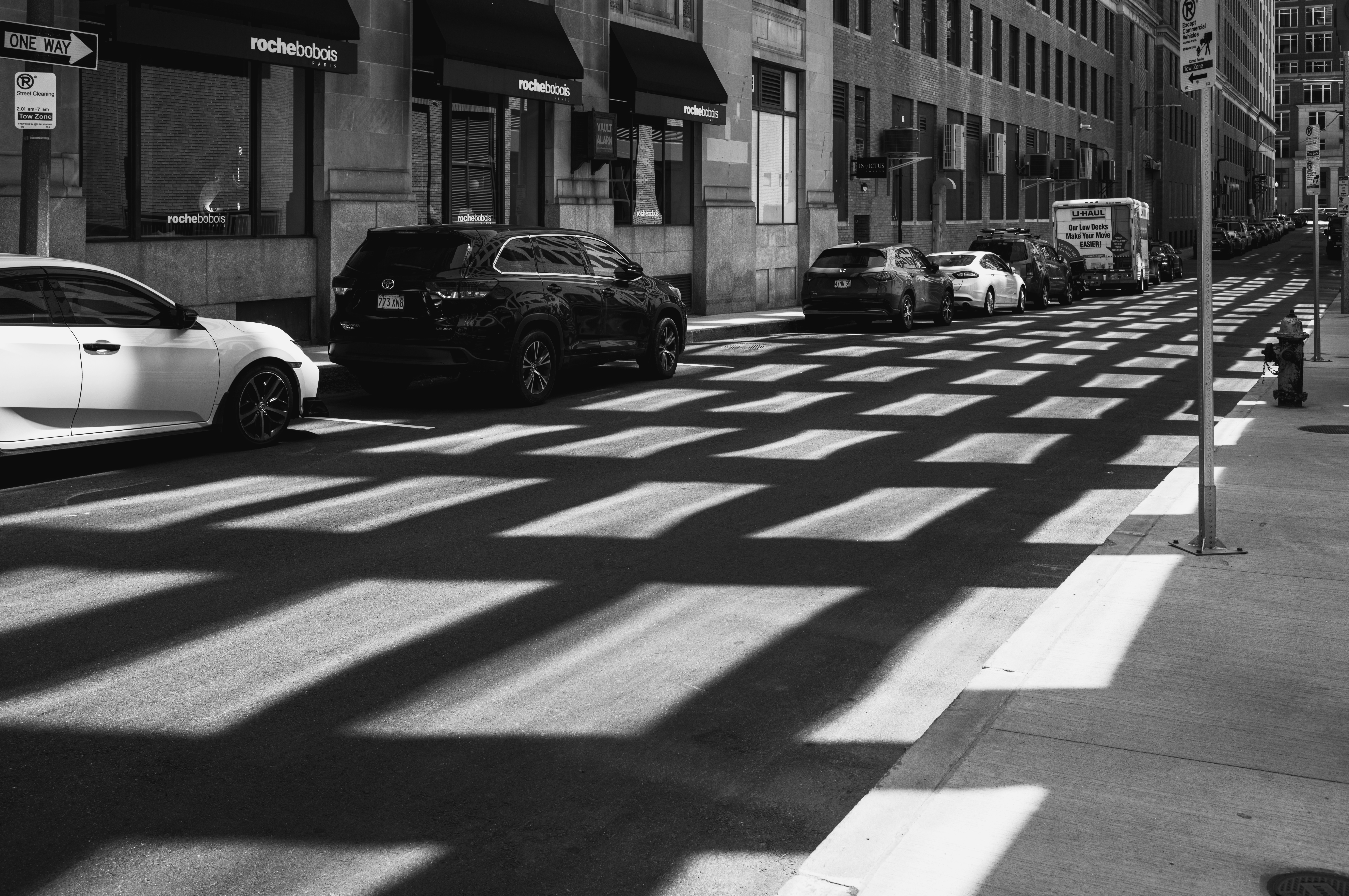 Rua da cidade com carros e sombras com padrões na faixa de pedestres