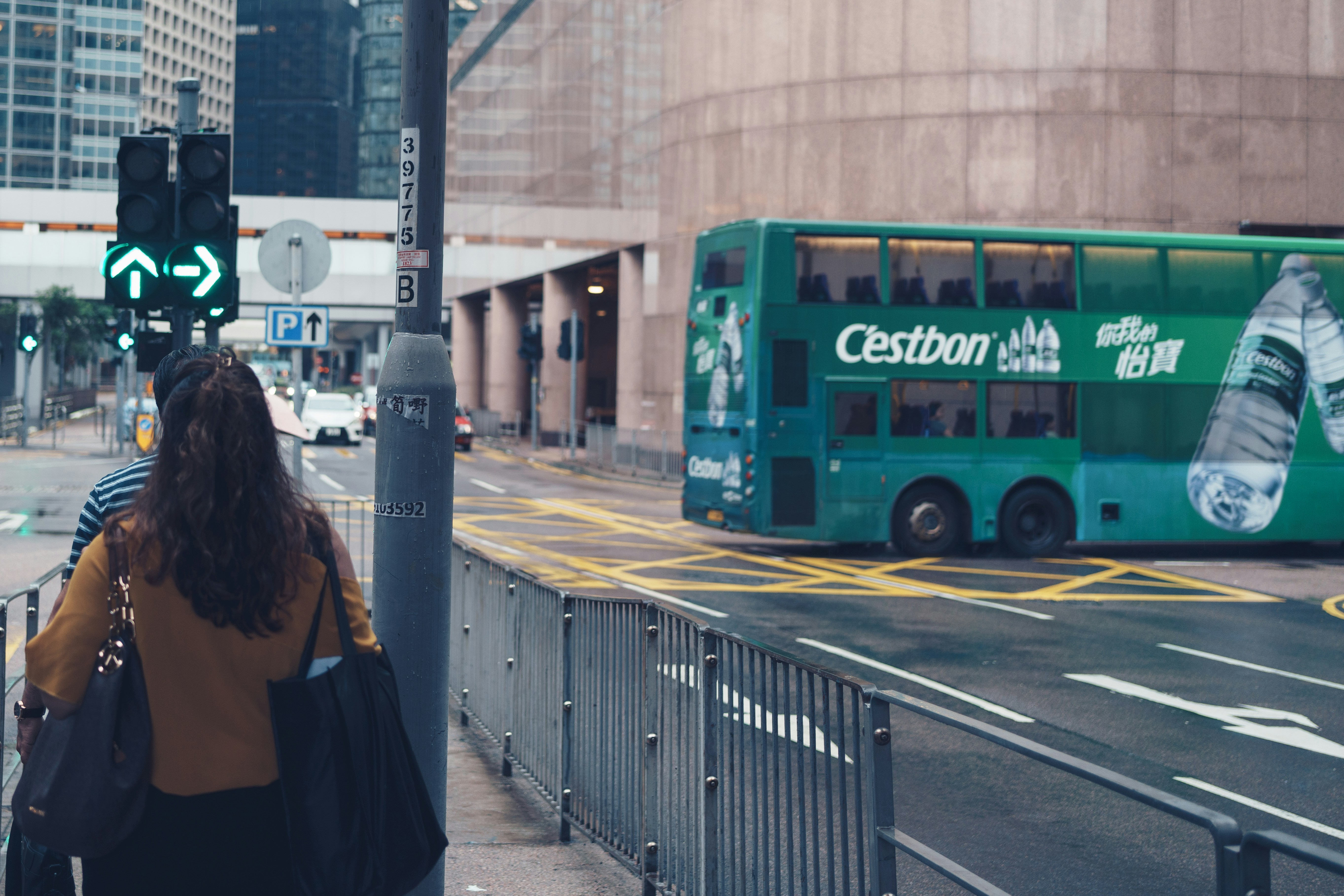 Woman walks past green double-decker bus on city street.