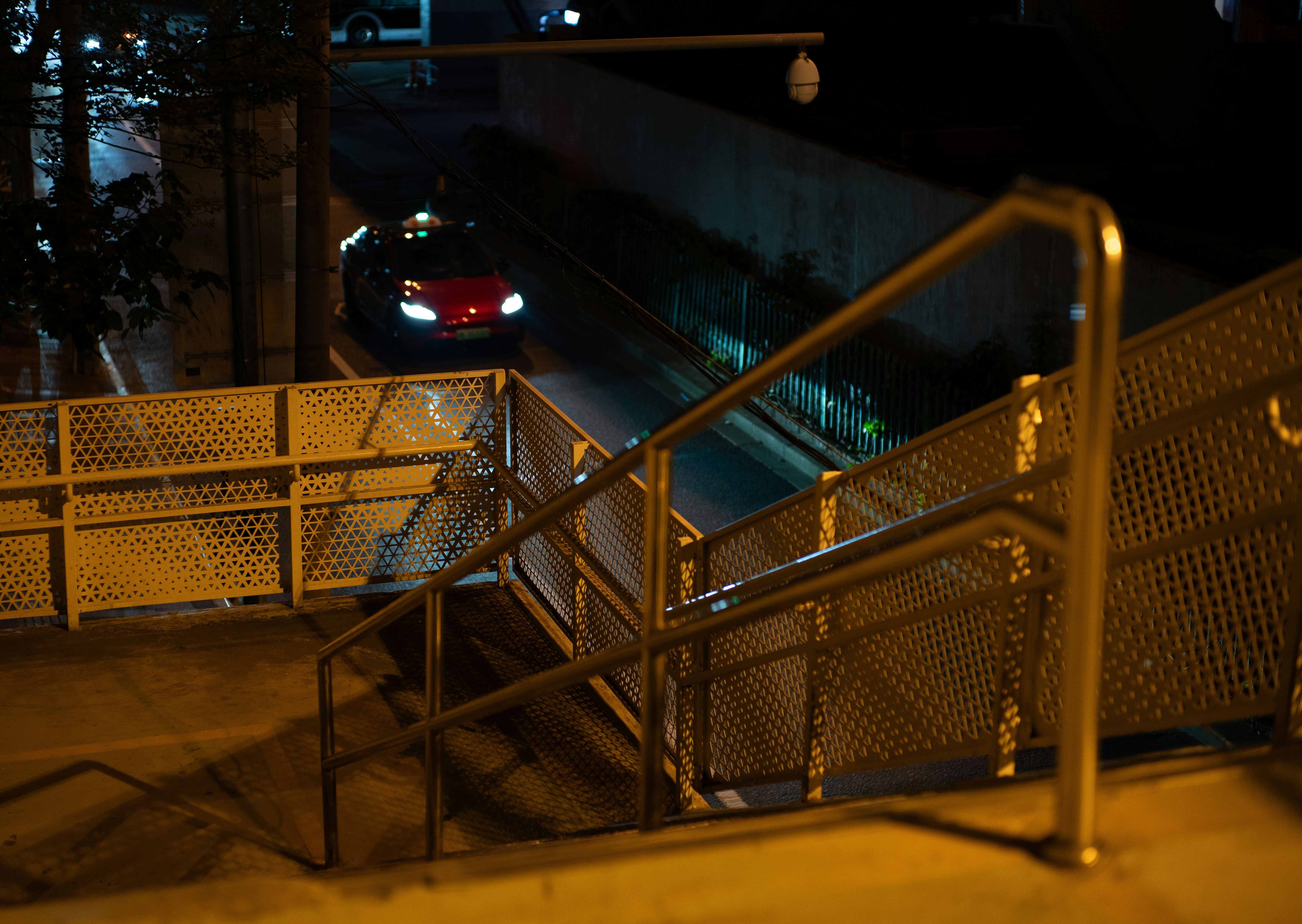A red car drives past a metal staircase at night.