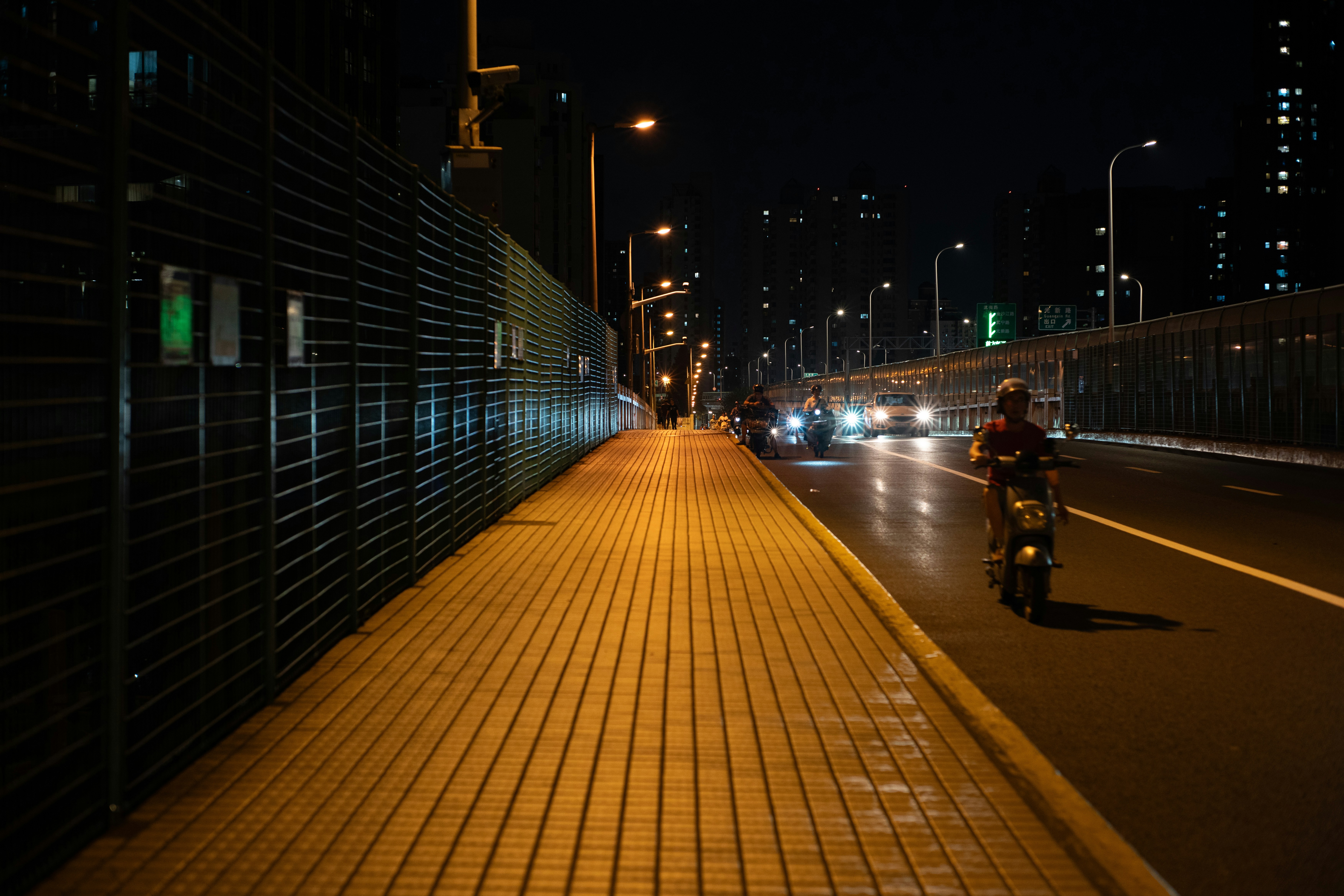 Illuminated city street at night with sidewalk and passing vehicles.