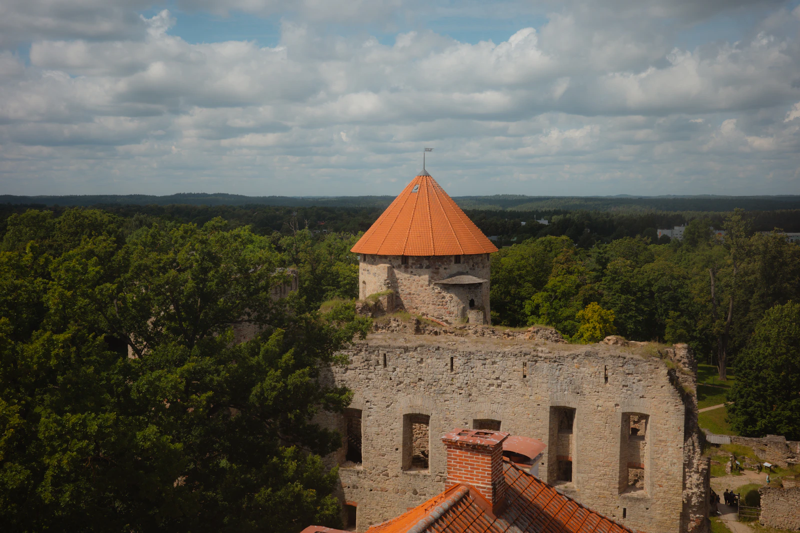 The tower of Cēsis castle with its orange roof above the forest