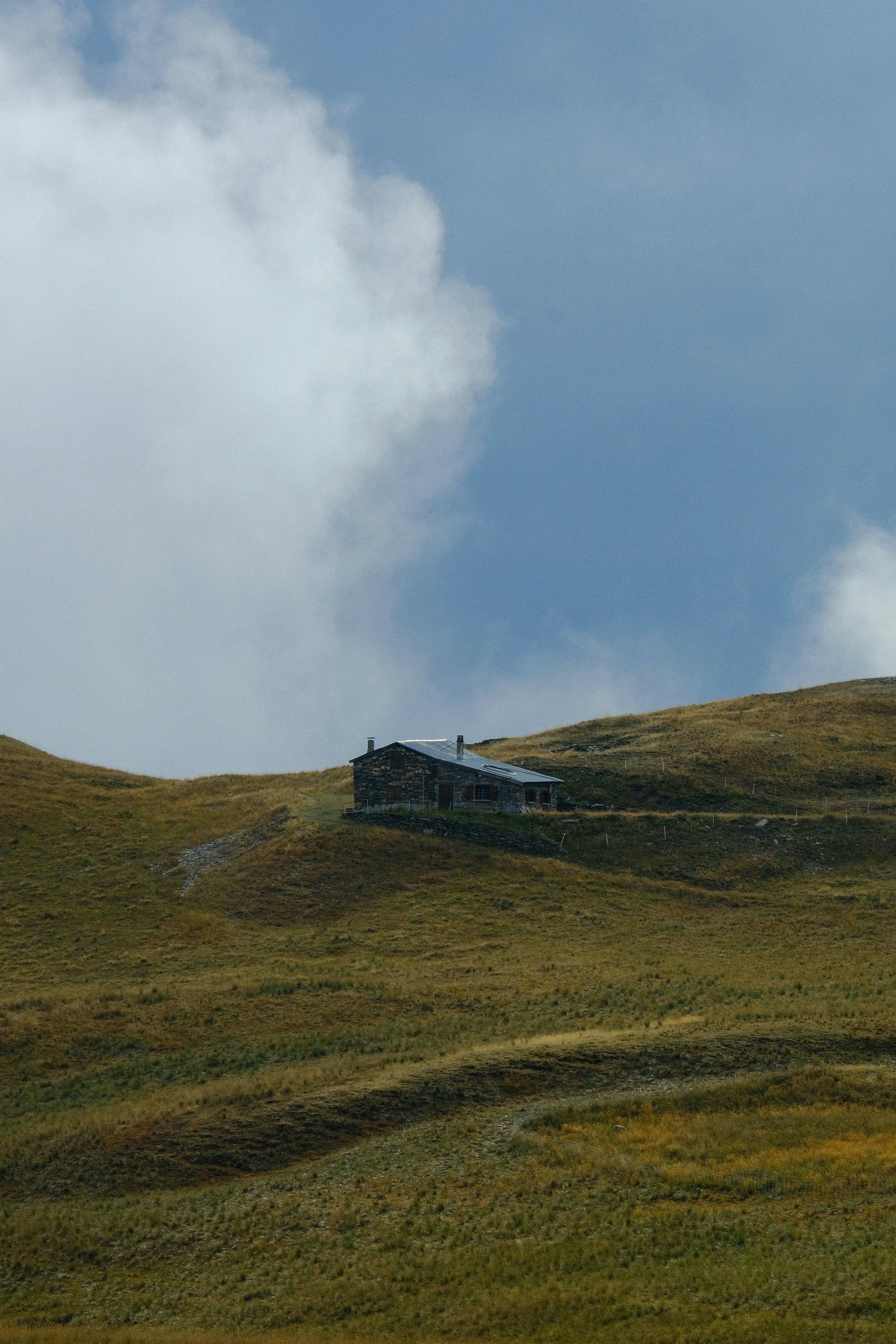 An old stone house on a grassy hill with clouds