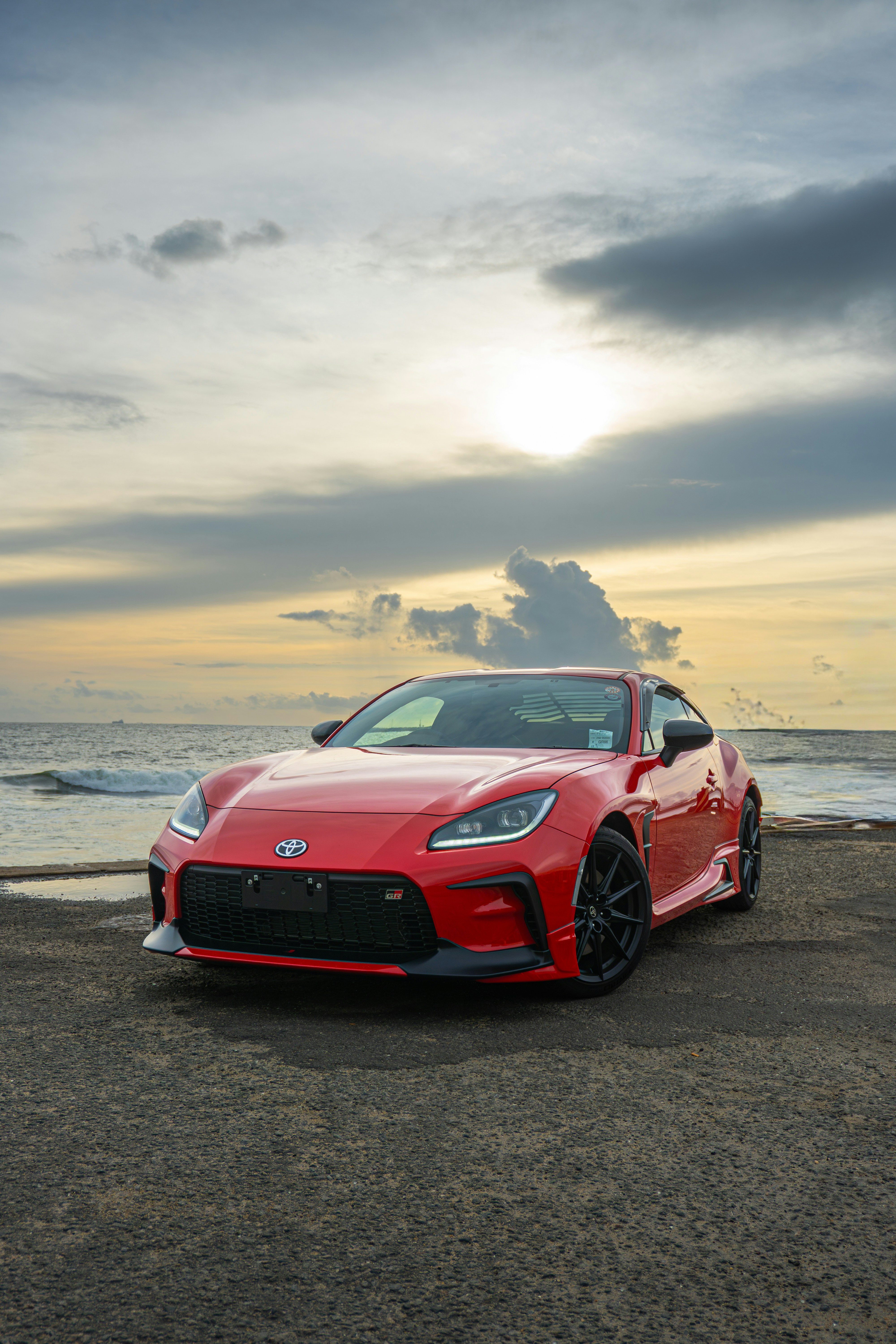 A red sports car parked by the ocean at sunset