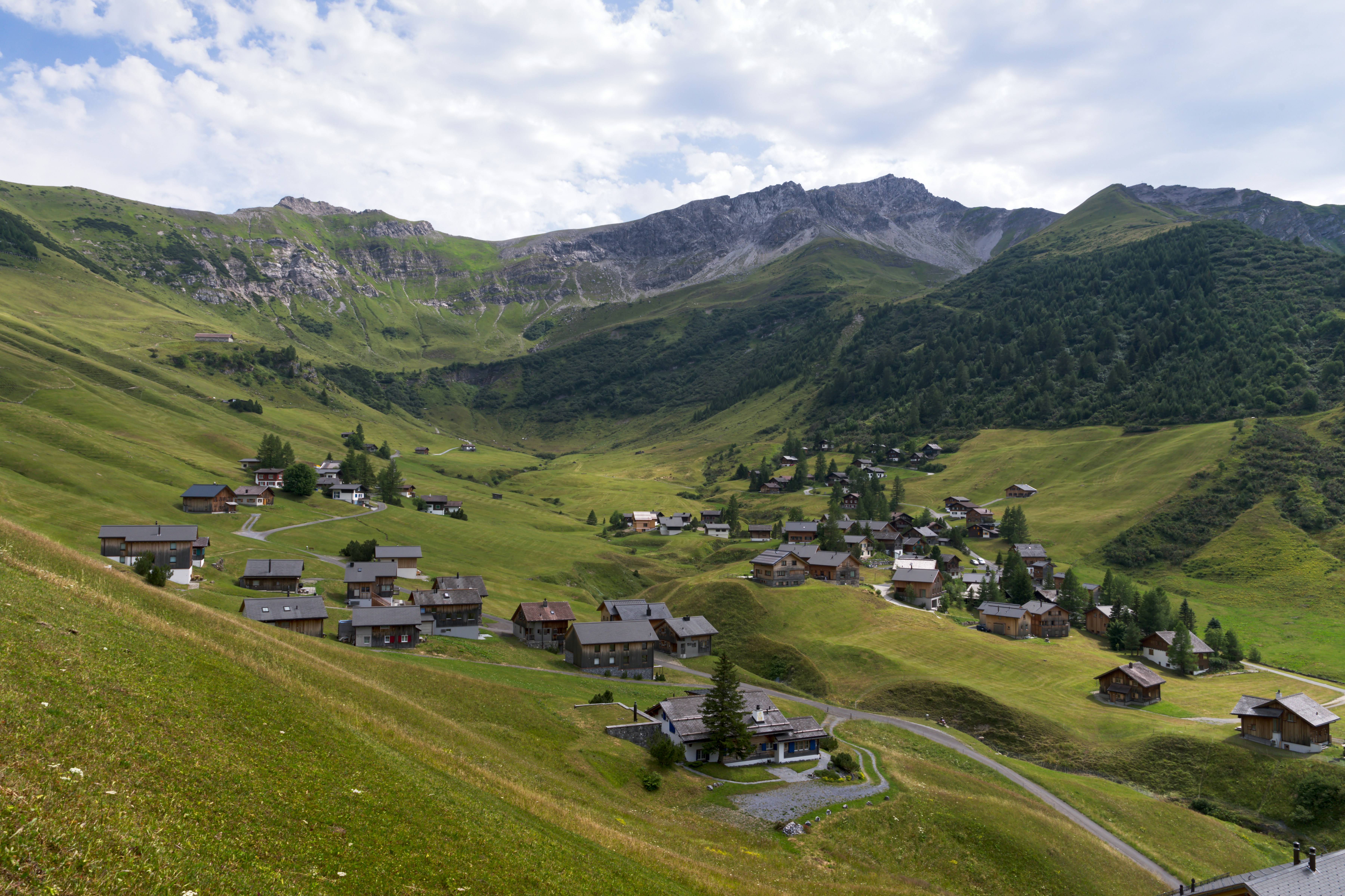 Villaggio alpino in una valle verde circondata da montagne.