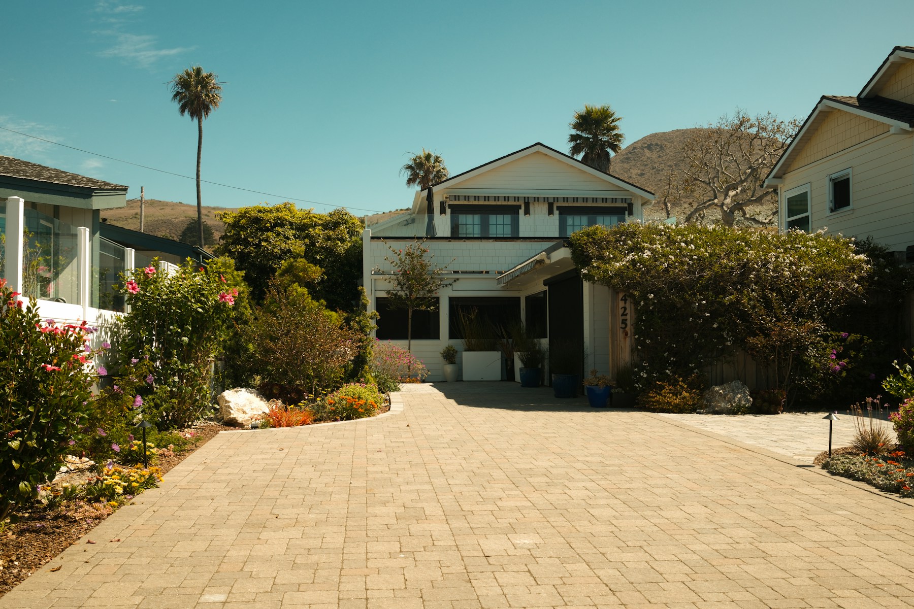 White house with a long paved driveway and green landscaping under a sunny sky