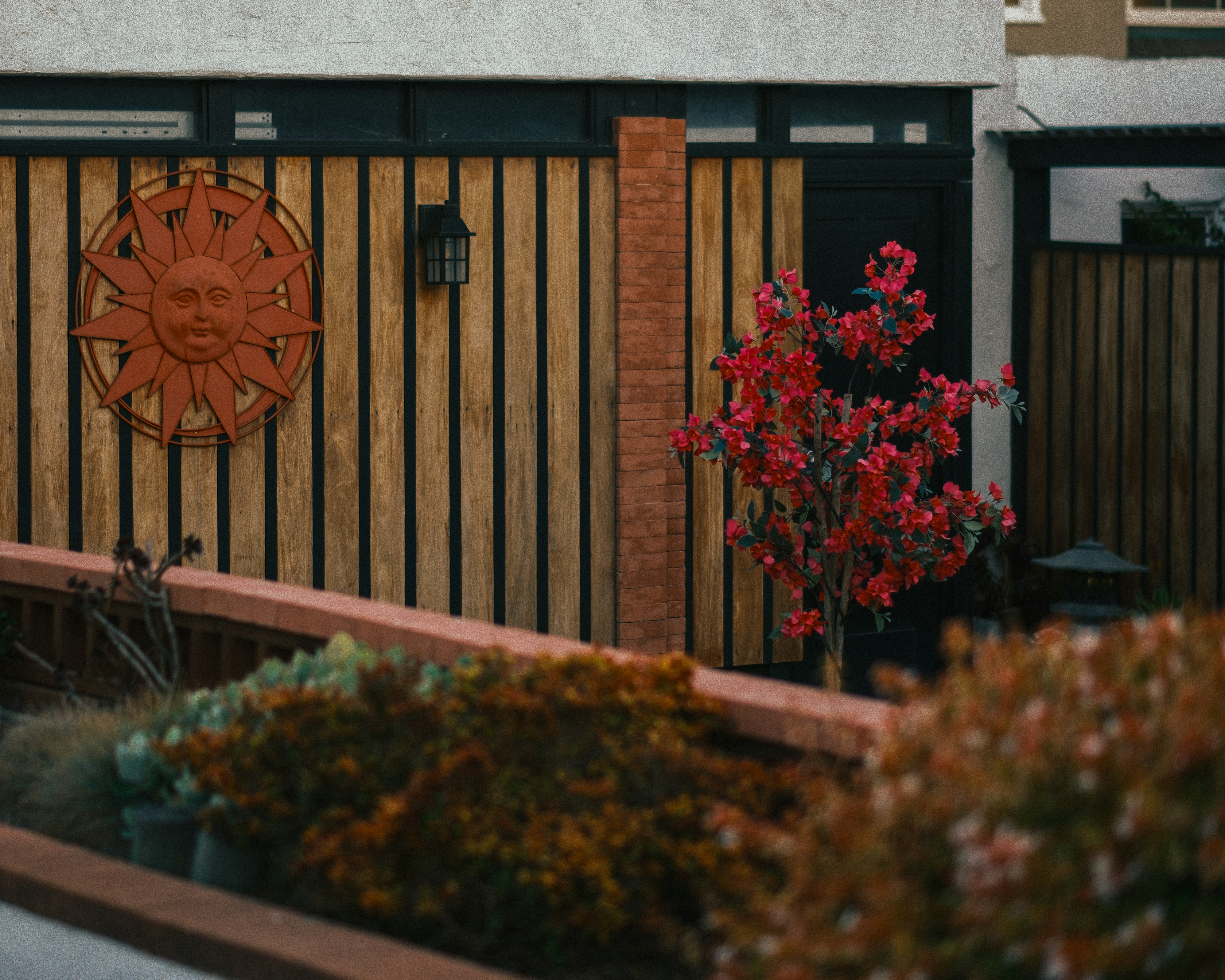 Wooden fence with sun decoration and vibrant red tree.