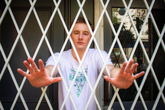 A man with hands pressed against a white diamond gate