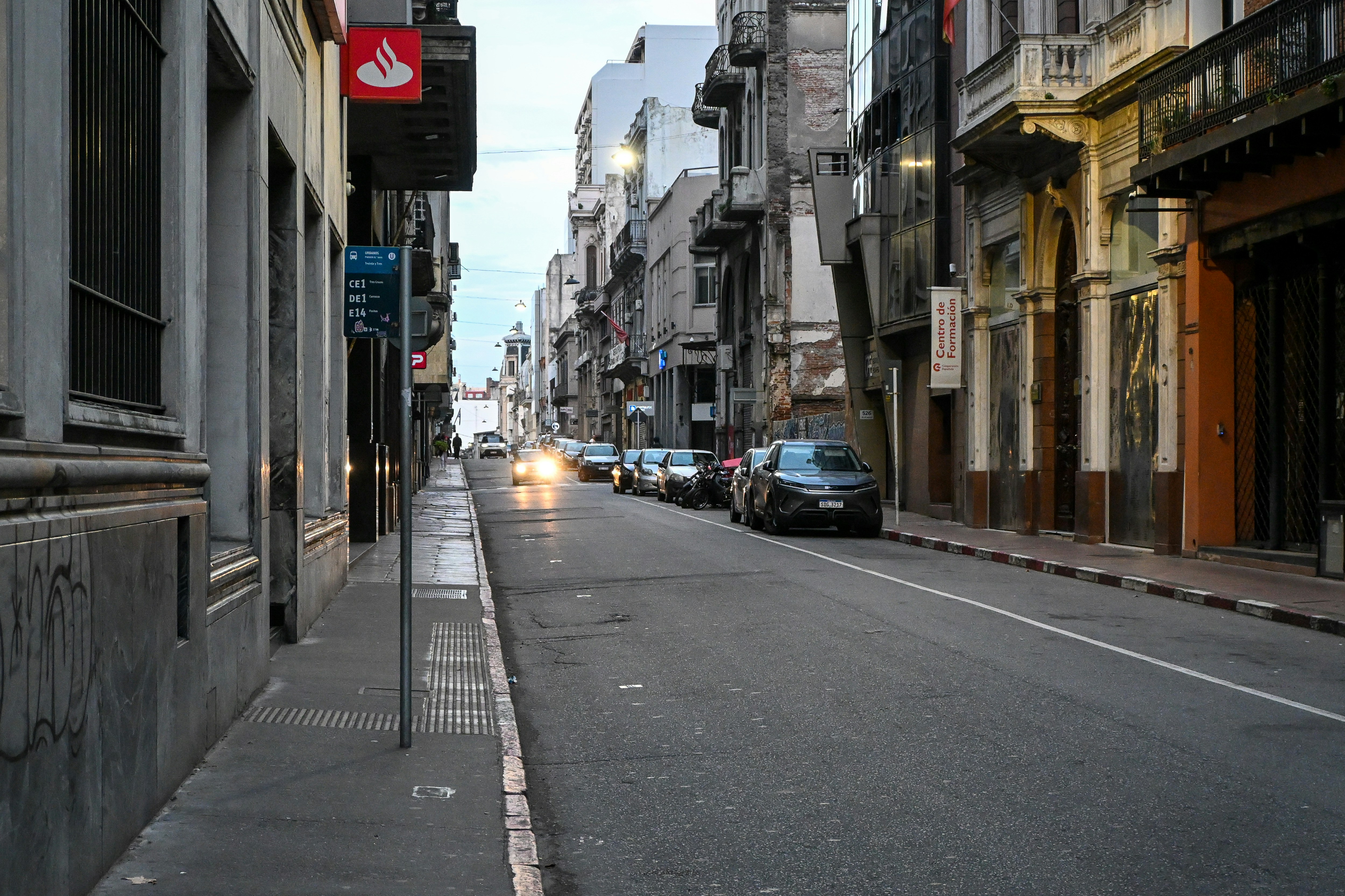 Urban street lined with buildings and parked cars at dusk.