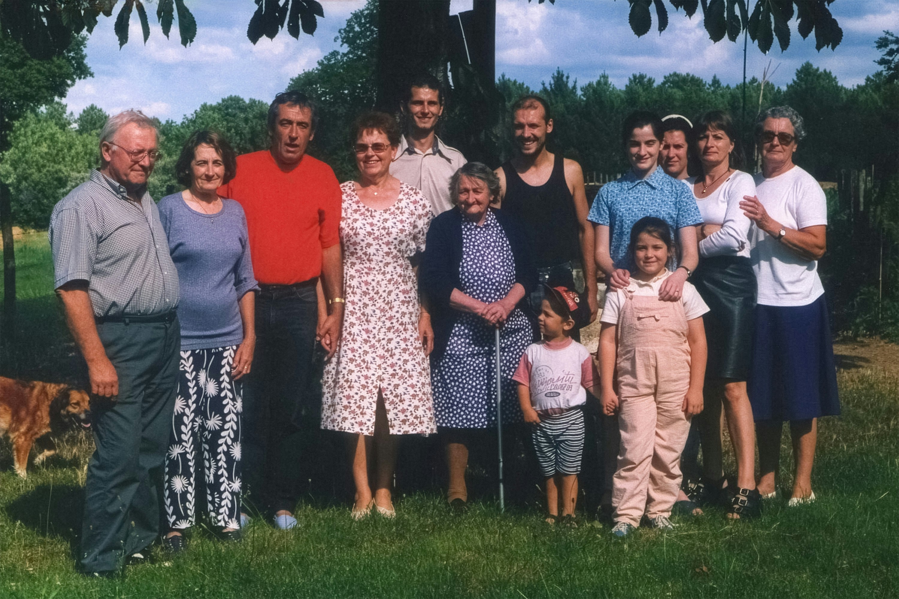 A multi-generational family stands together on a sunny lawn.