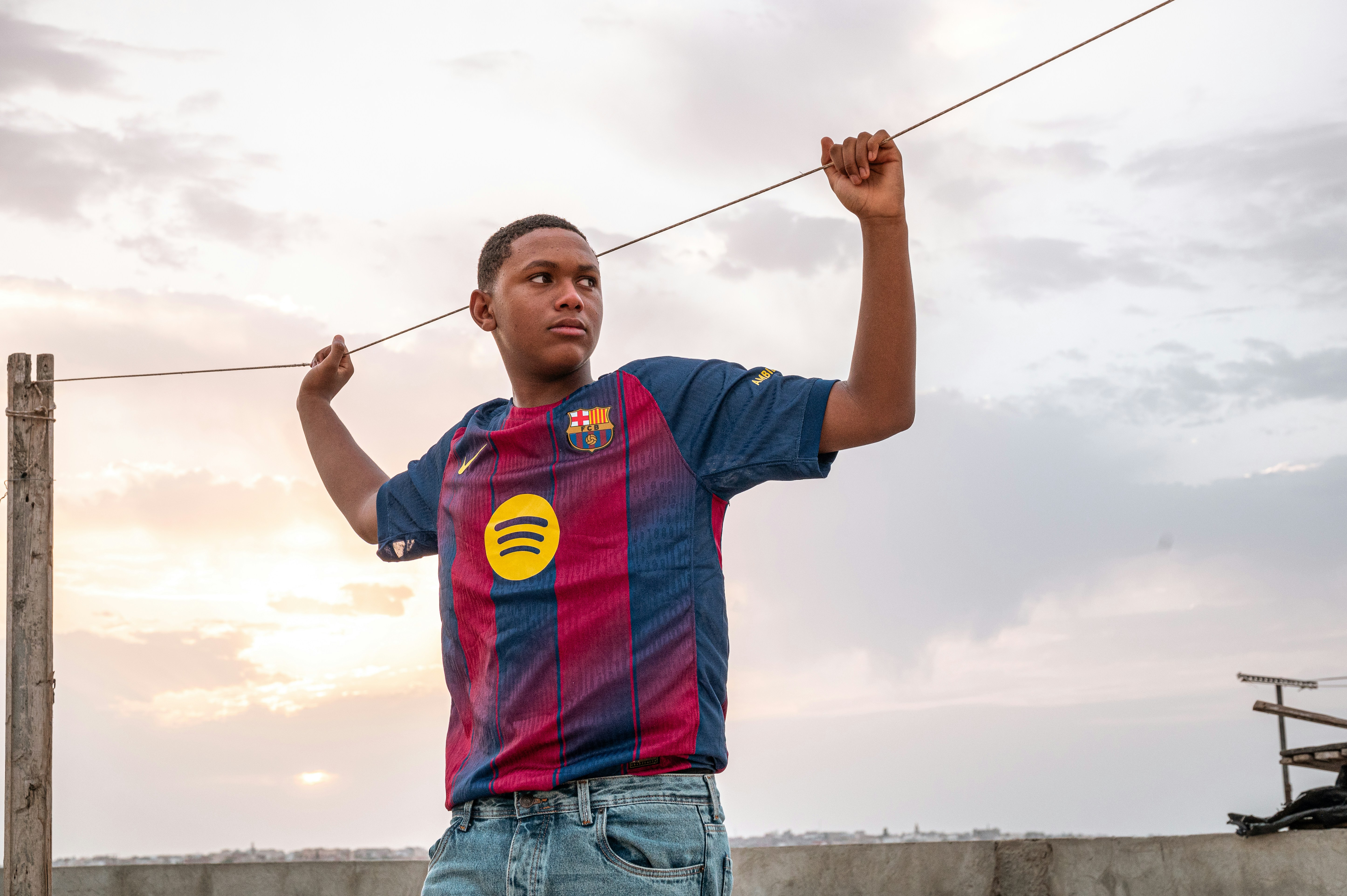 Pemuda berbaju jersey memegang garis melawan langit cerah.