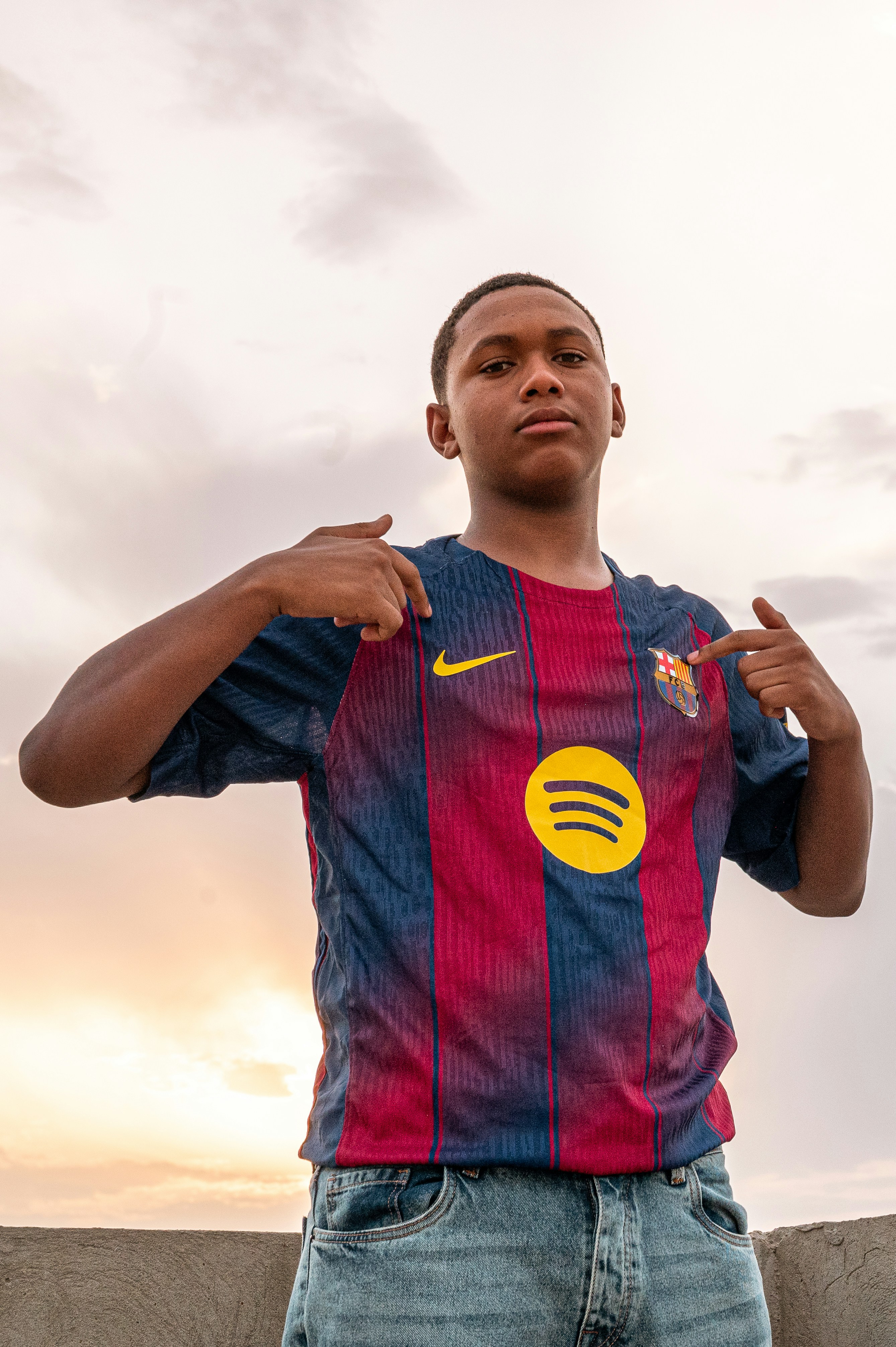 Seorang pemuda dengan bangga menunjuk ke jersey sepak bola bergarisnya.