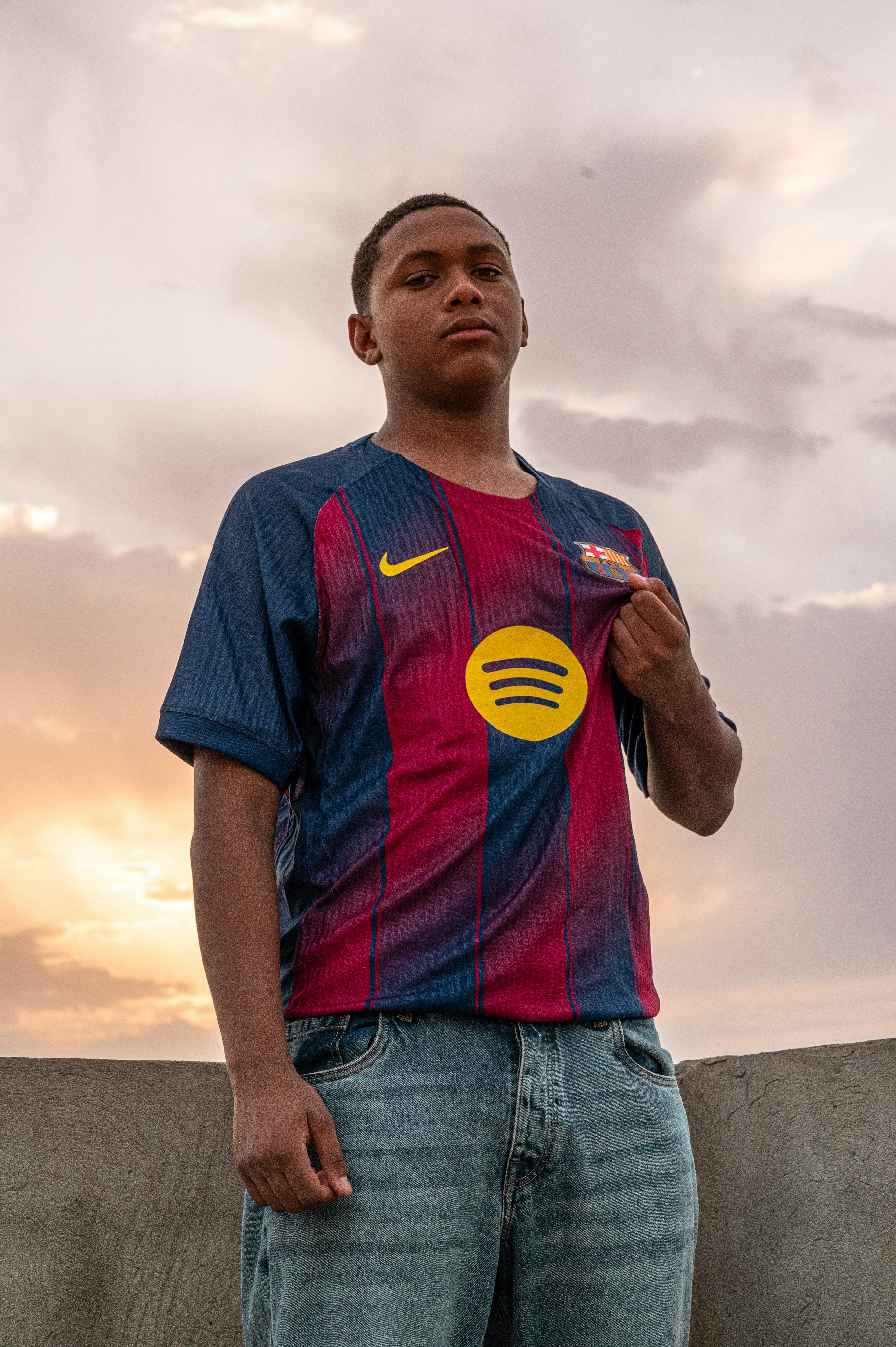 Pria muda mengenakan jersey Barcelona dan celana jeans saat matahari terbenam.