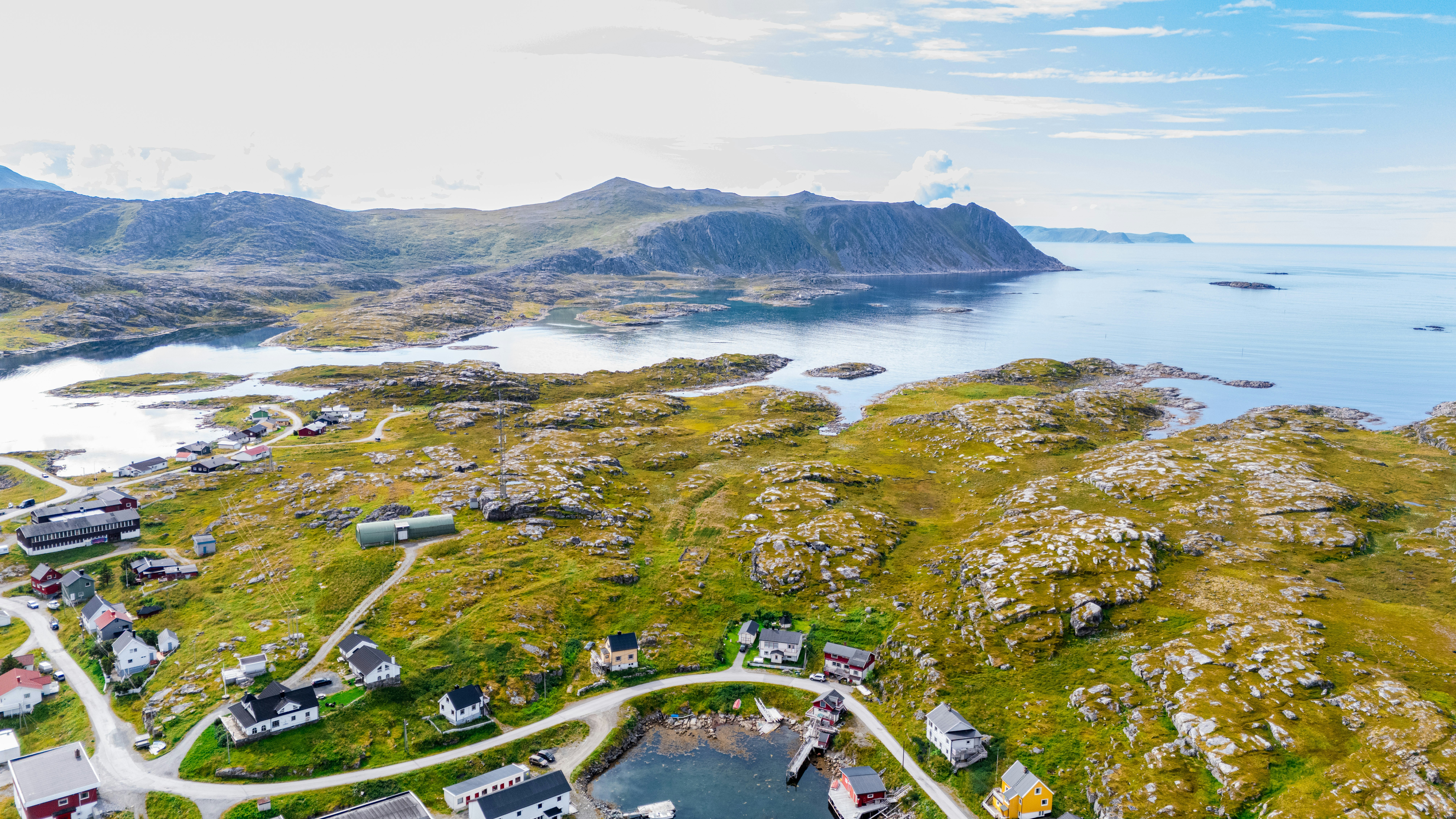 Coastal village with houses on green hills by the ocean.
