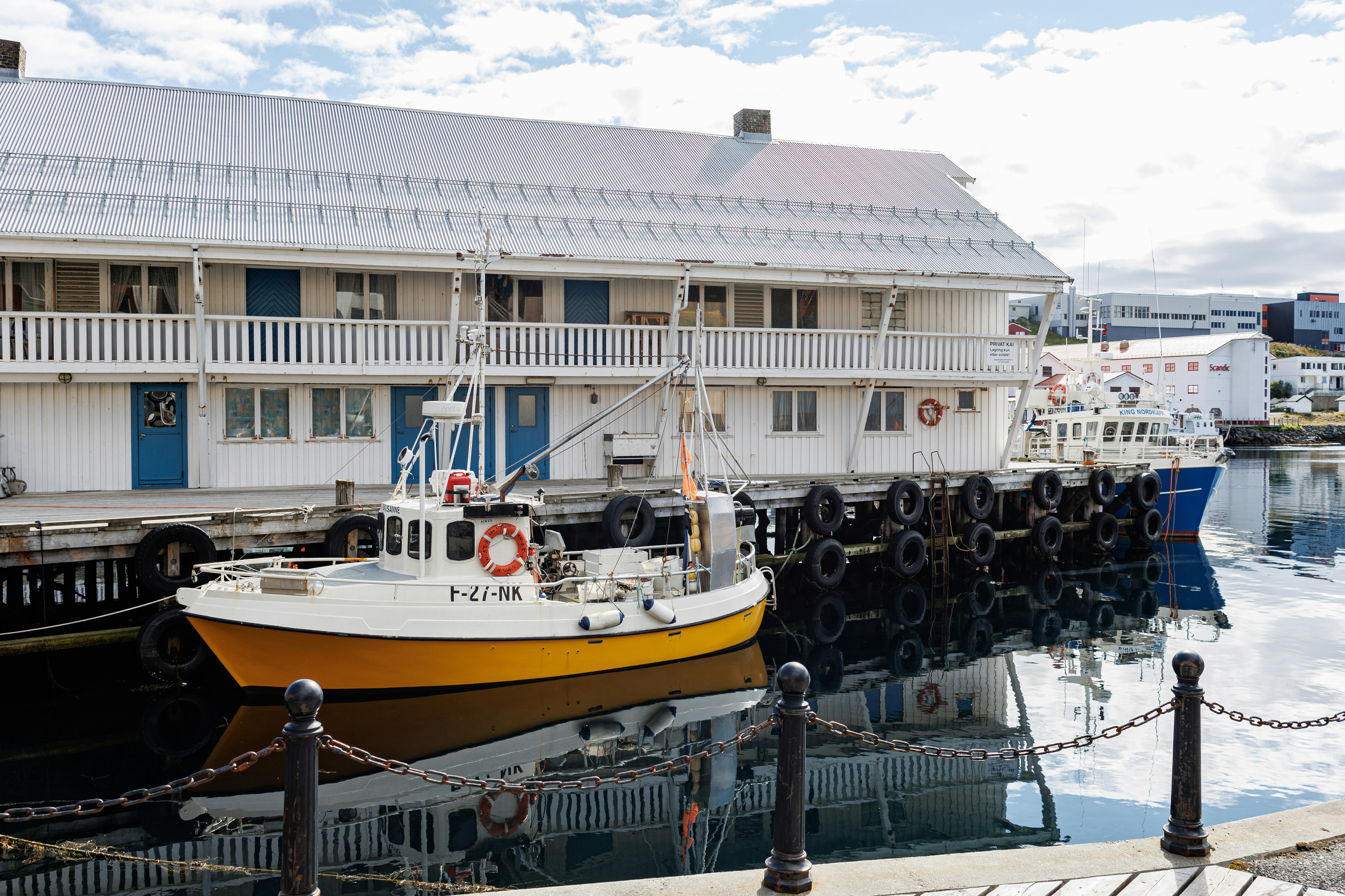 A yellow boat moored by a white waterside building.