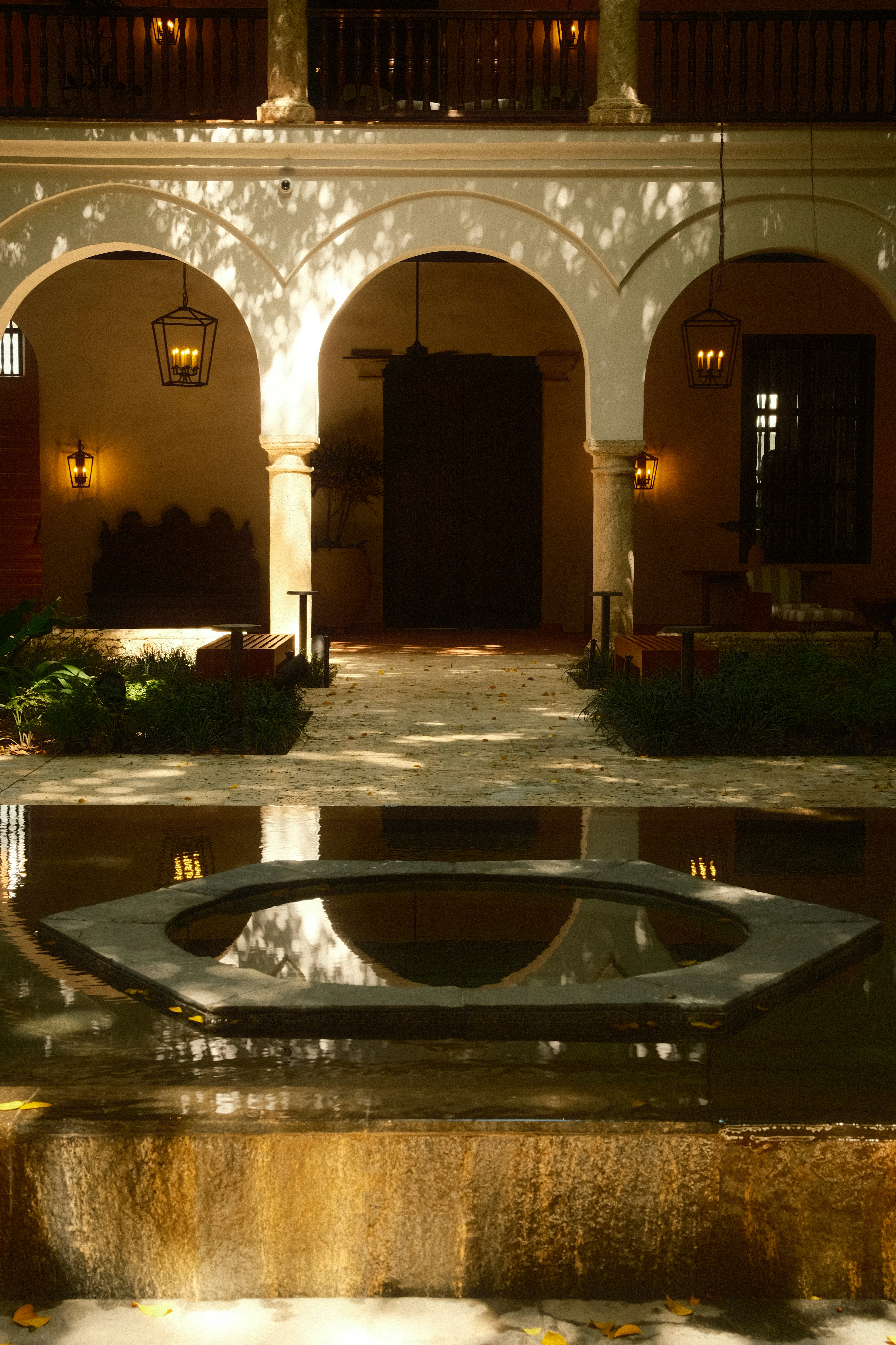 Colonial courtyard arcade with stone arches, hanging lanterns and dappled sunlight