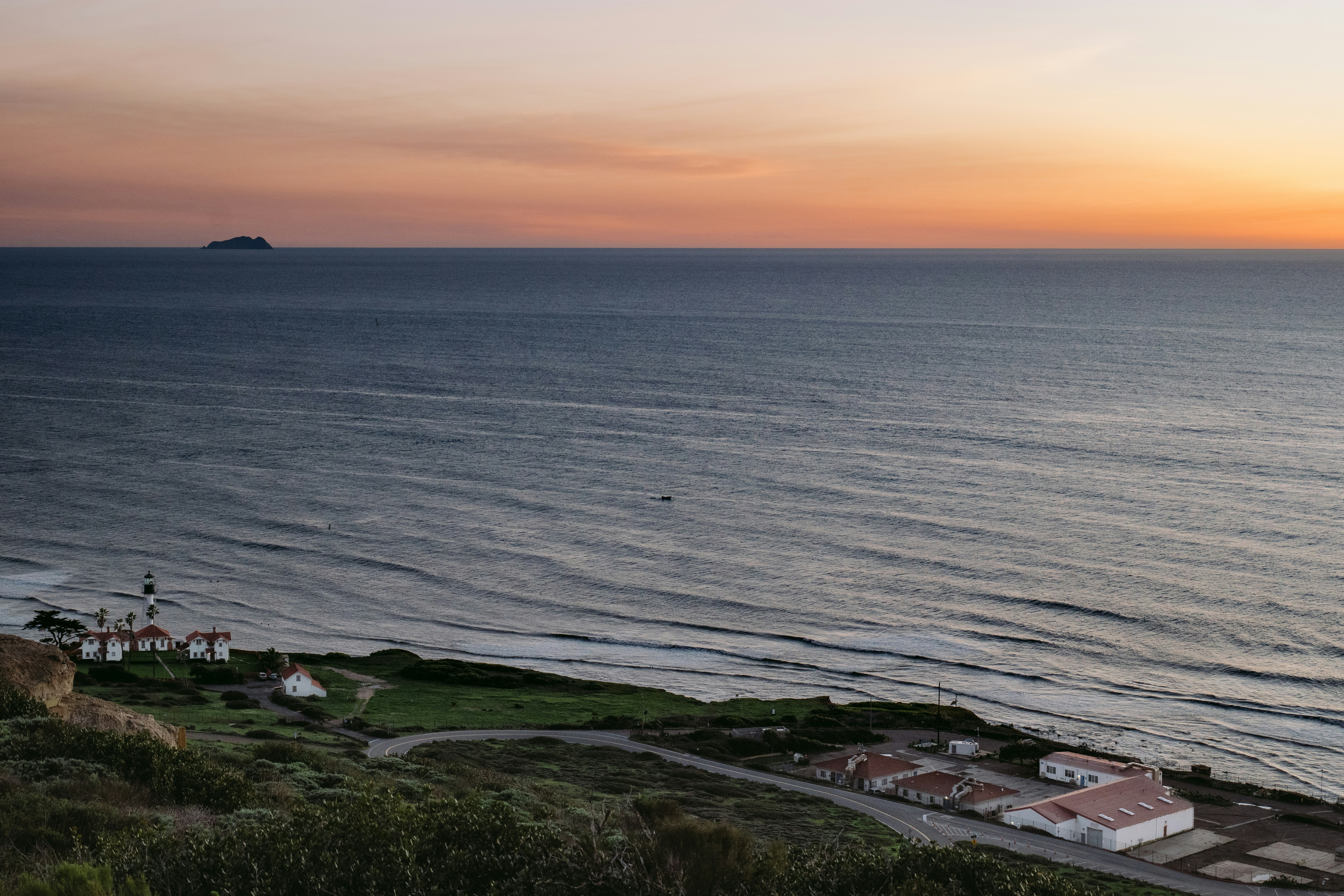 Sunset over a vast ocean with a coastline and buildings.