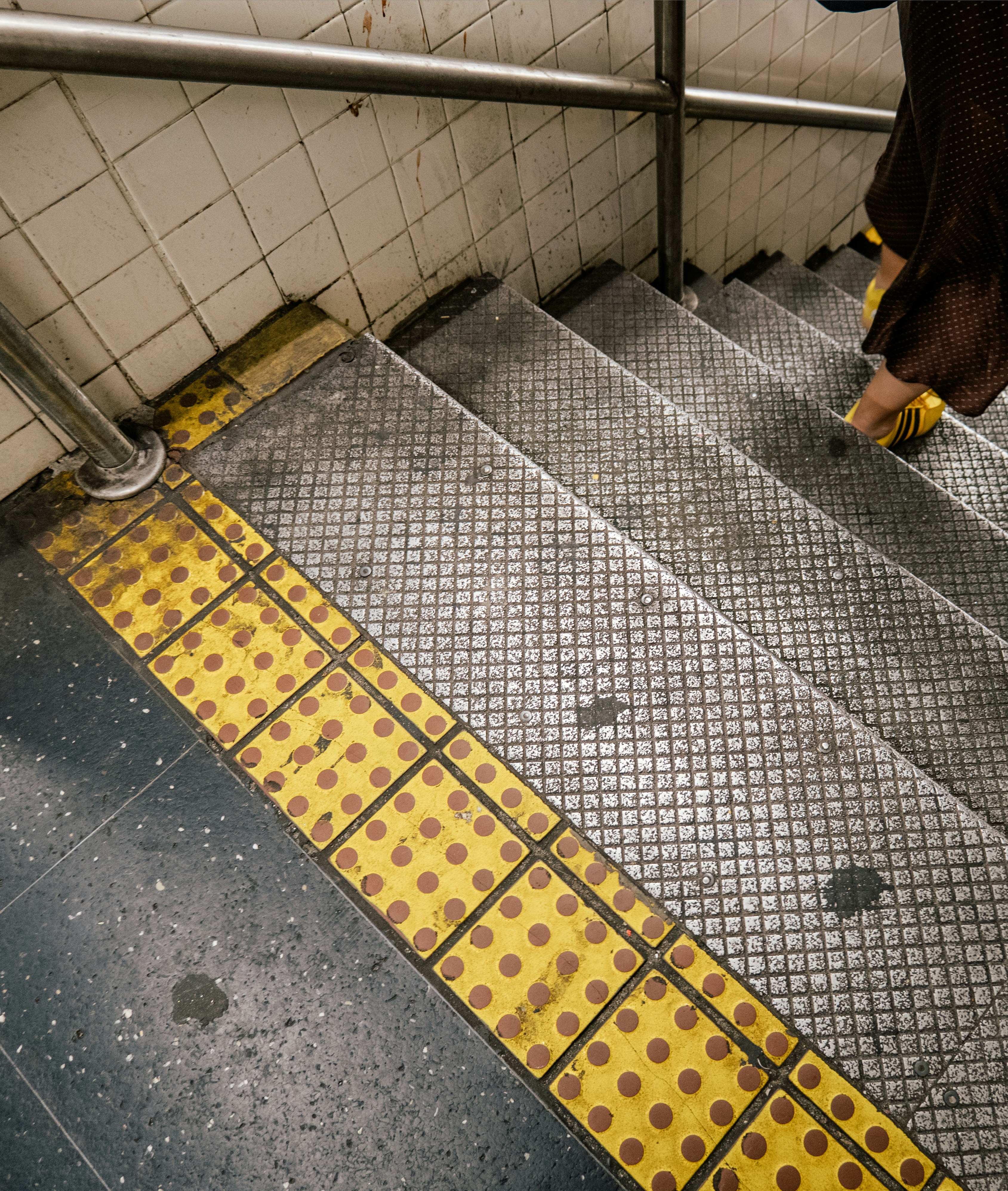 A person walks down metal stairs with yellow tactile paving.