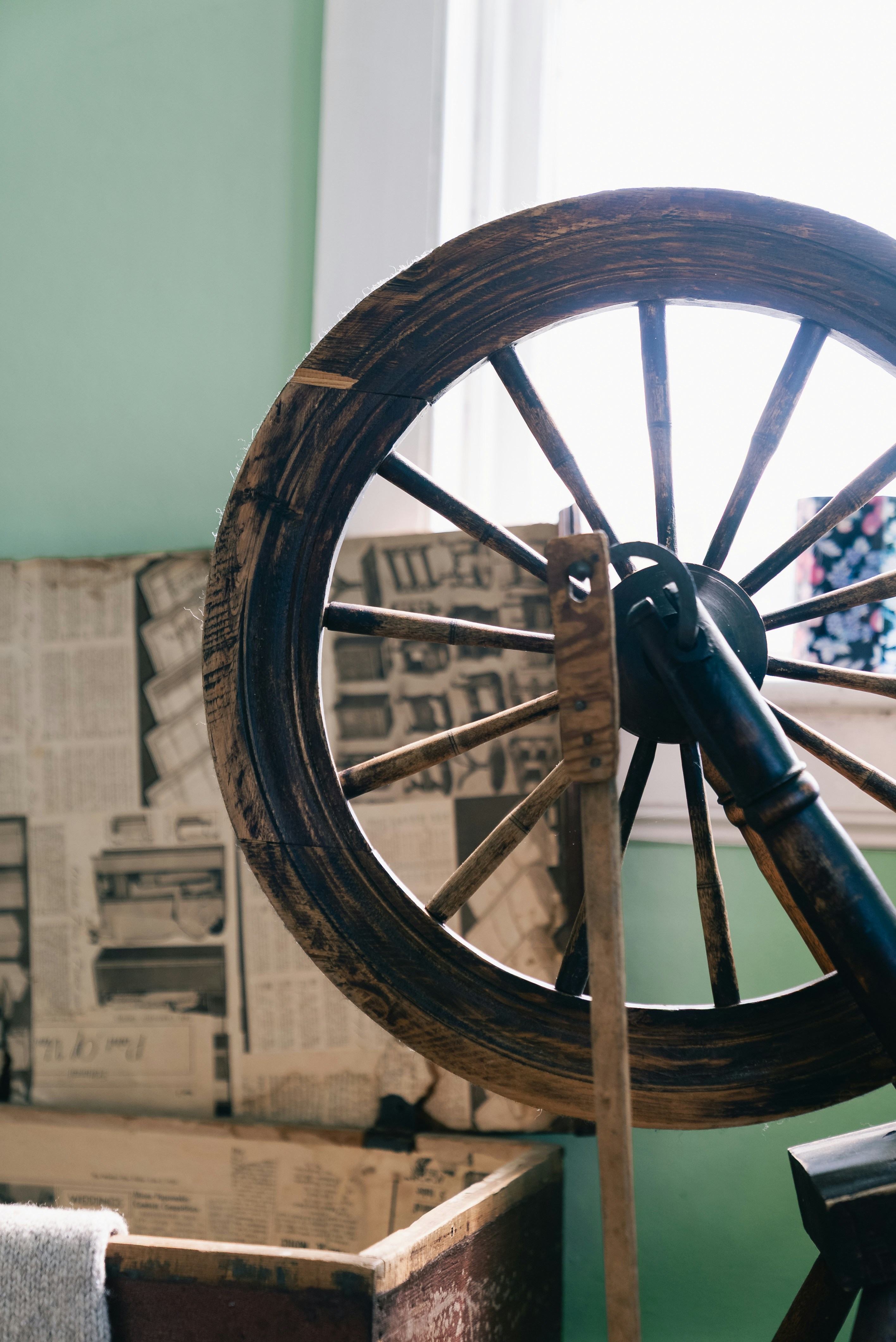 Antique wooden spinning wheel against a light green wall.