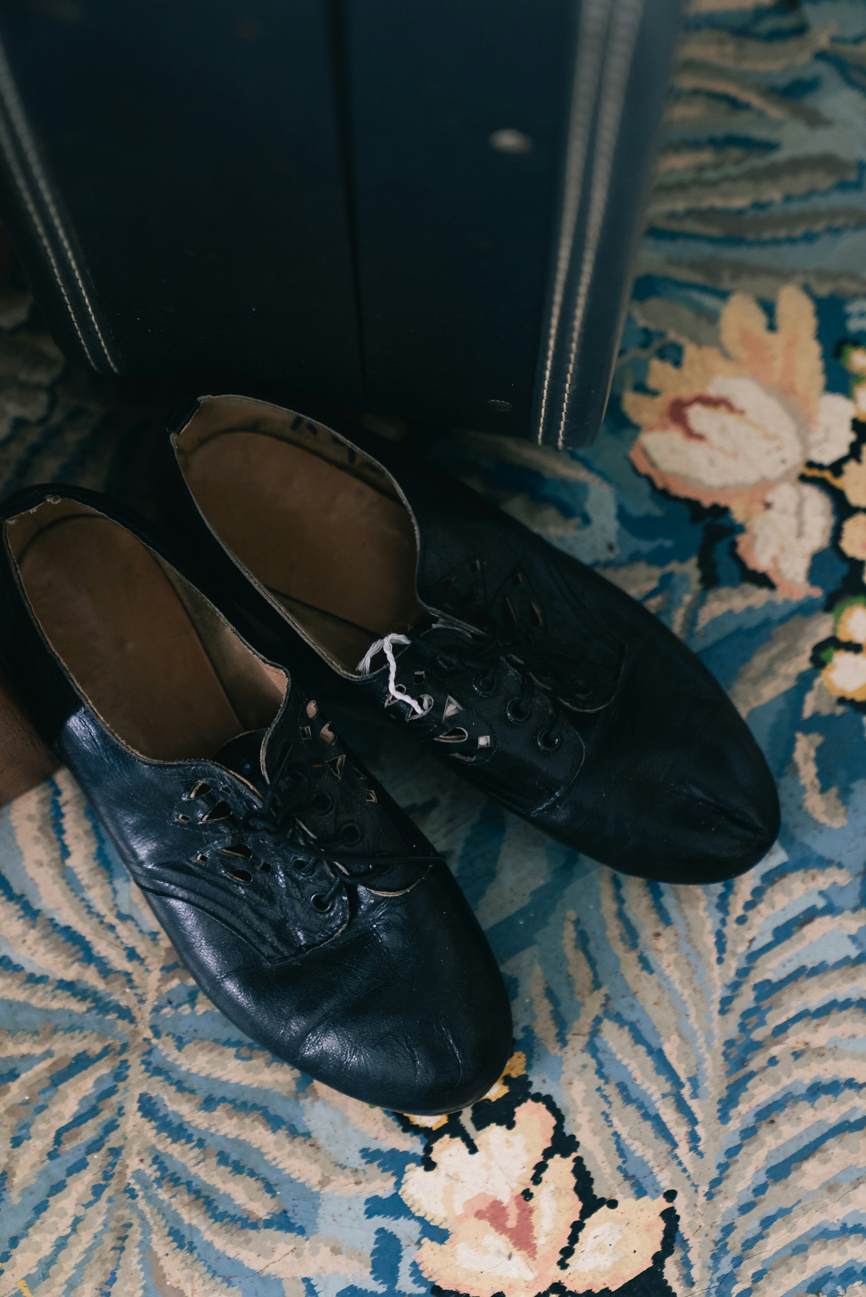 Two black dress shoes sit on a floral patterned rug.