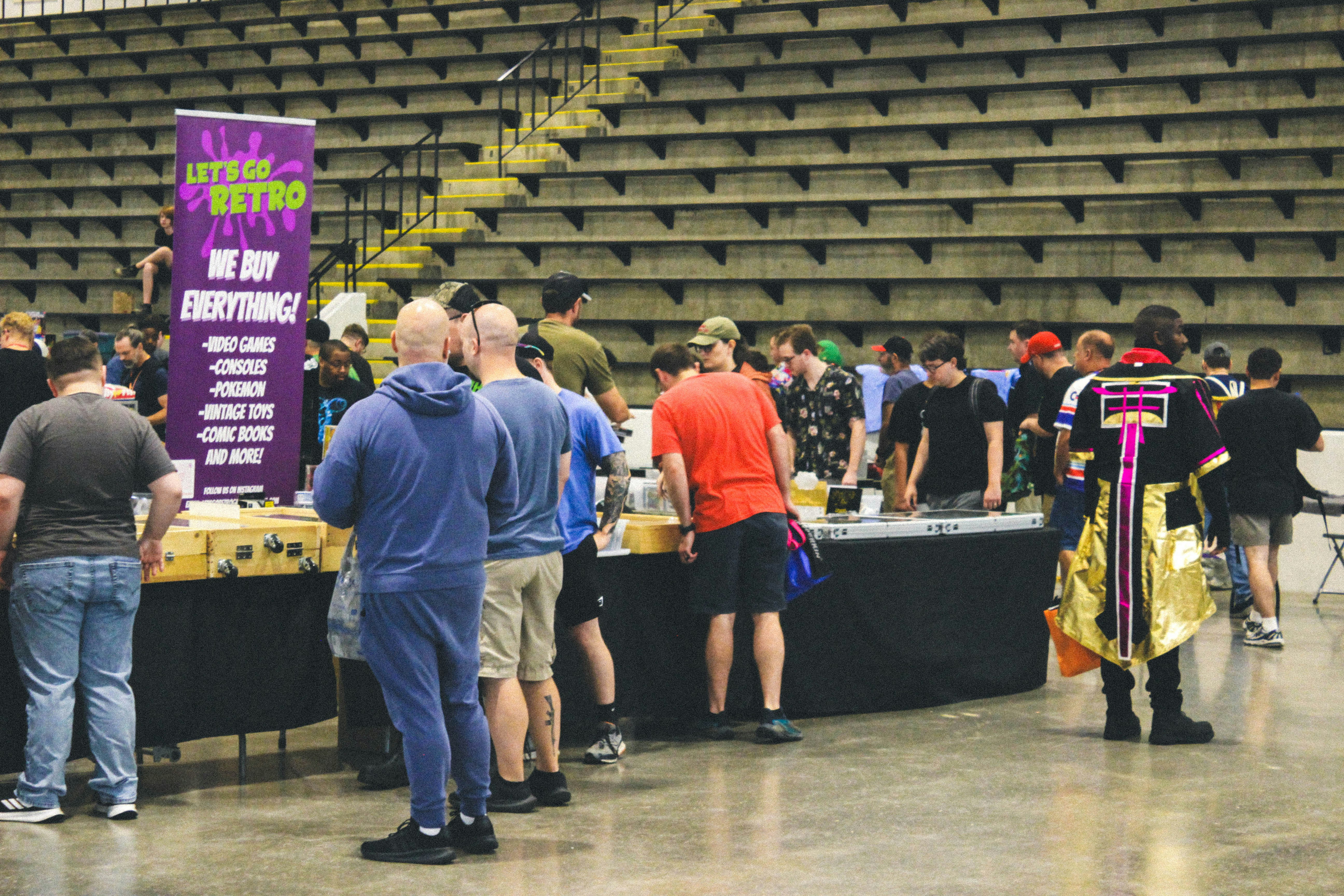 Attendees browsing vendor booths at an indoor convention with bleachers