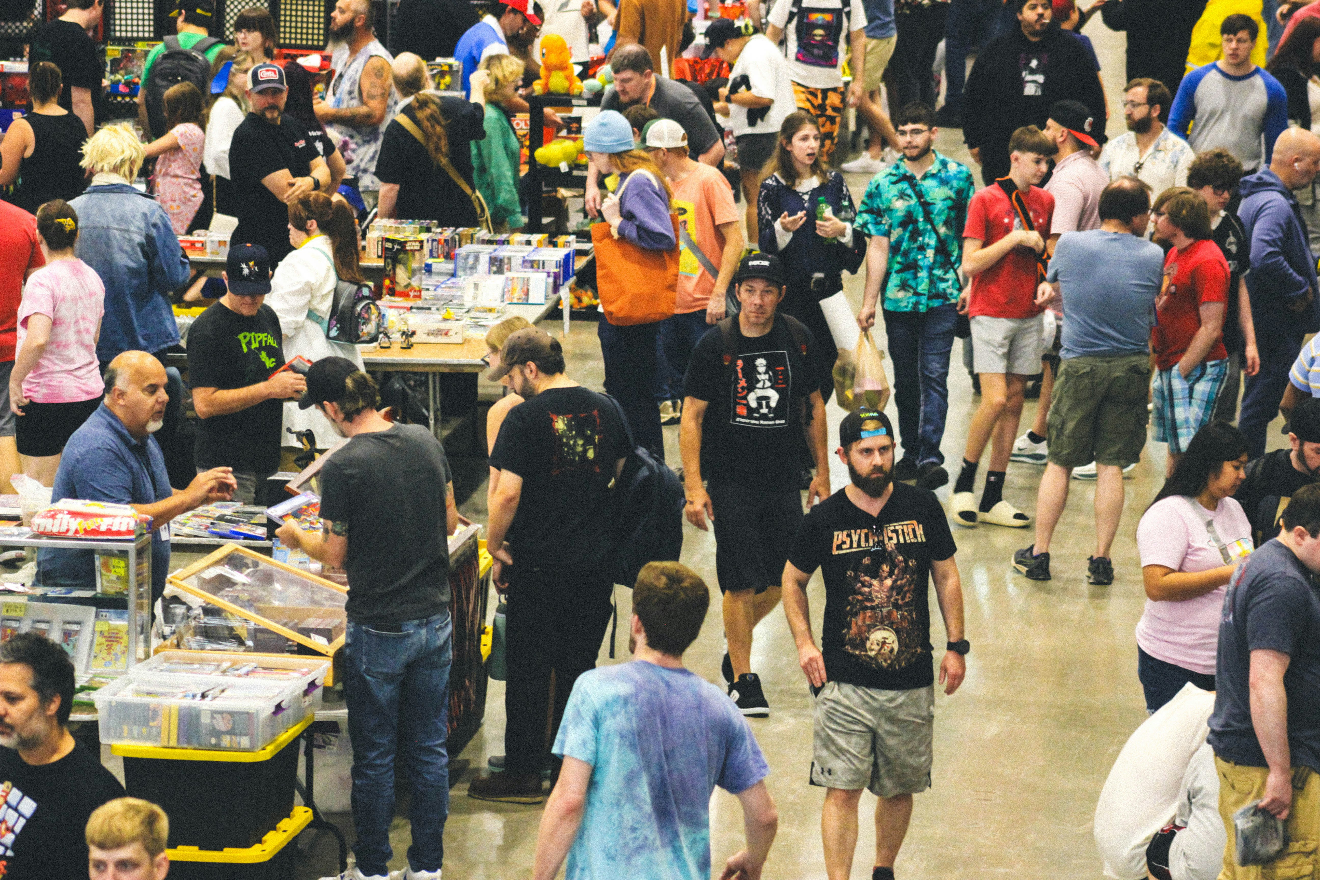 A bustling indoor event with numerous people browsing merchandise