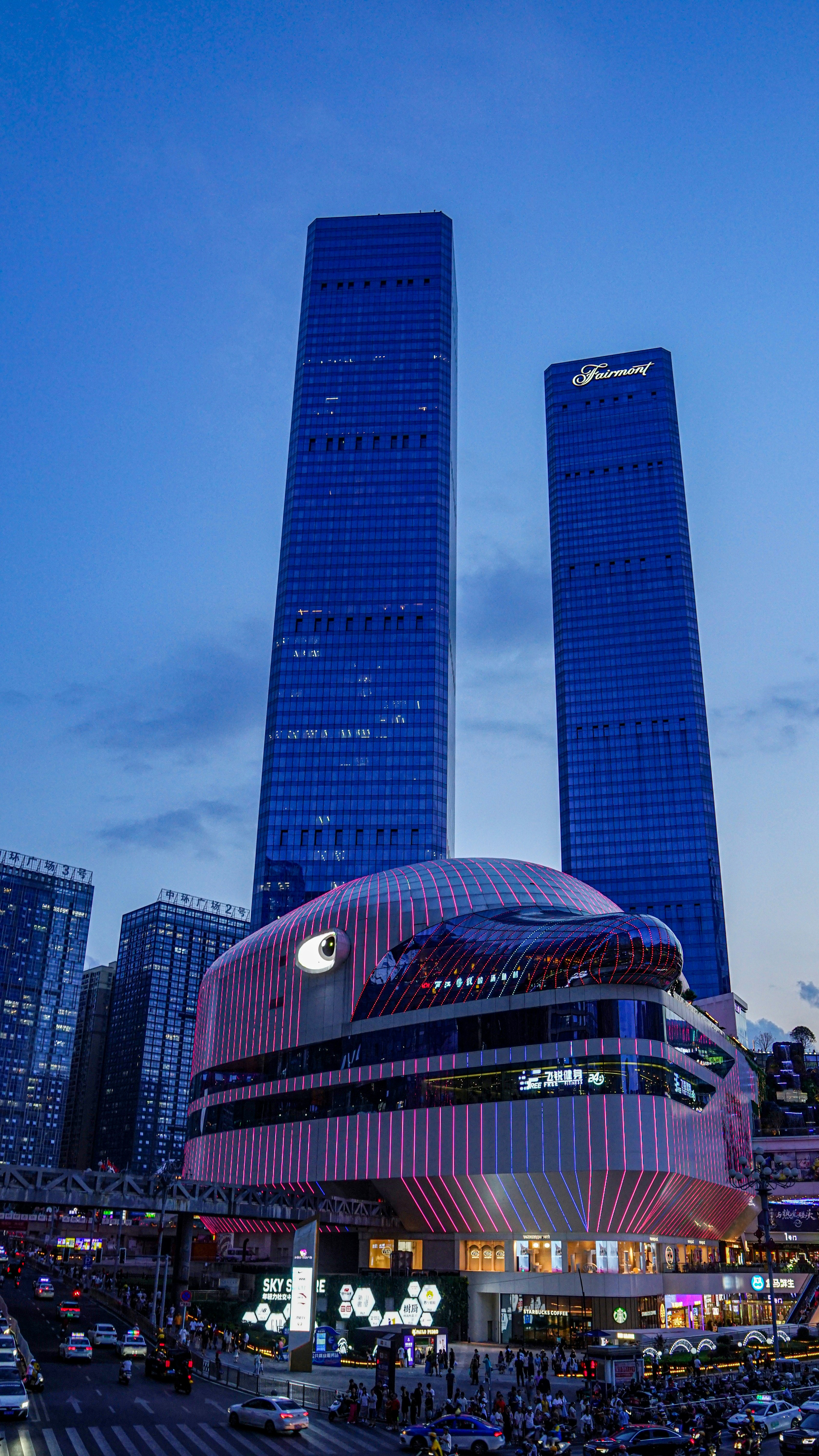 Edificio futurista con luces rosas y rascacielos azules al anochecer.