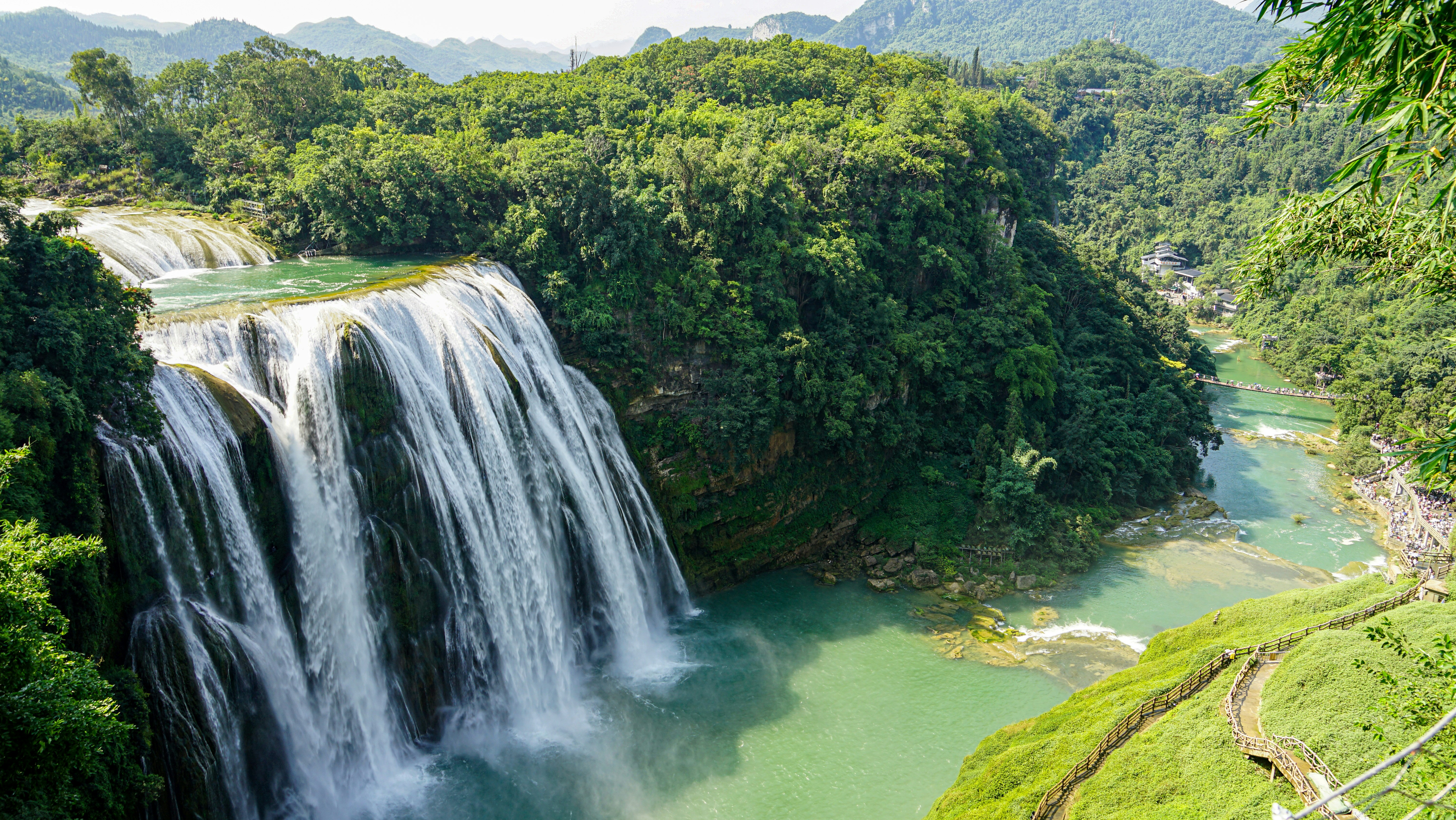 Majestuosa cascada y río turquesa rodeados de frondosos bosques verdes.