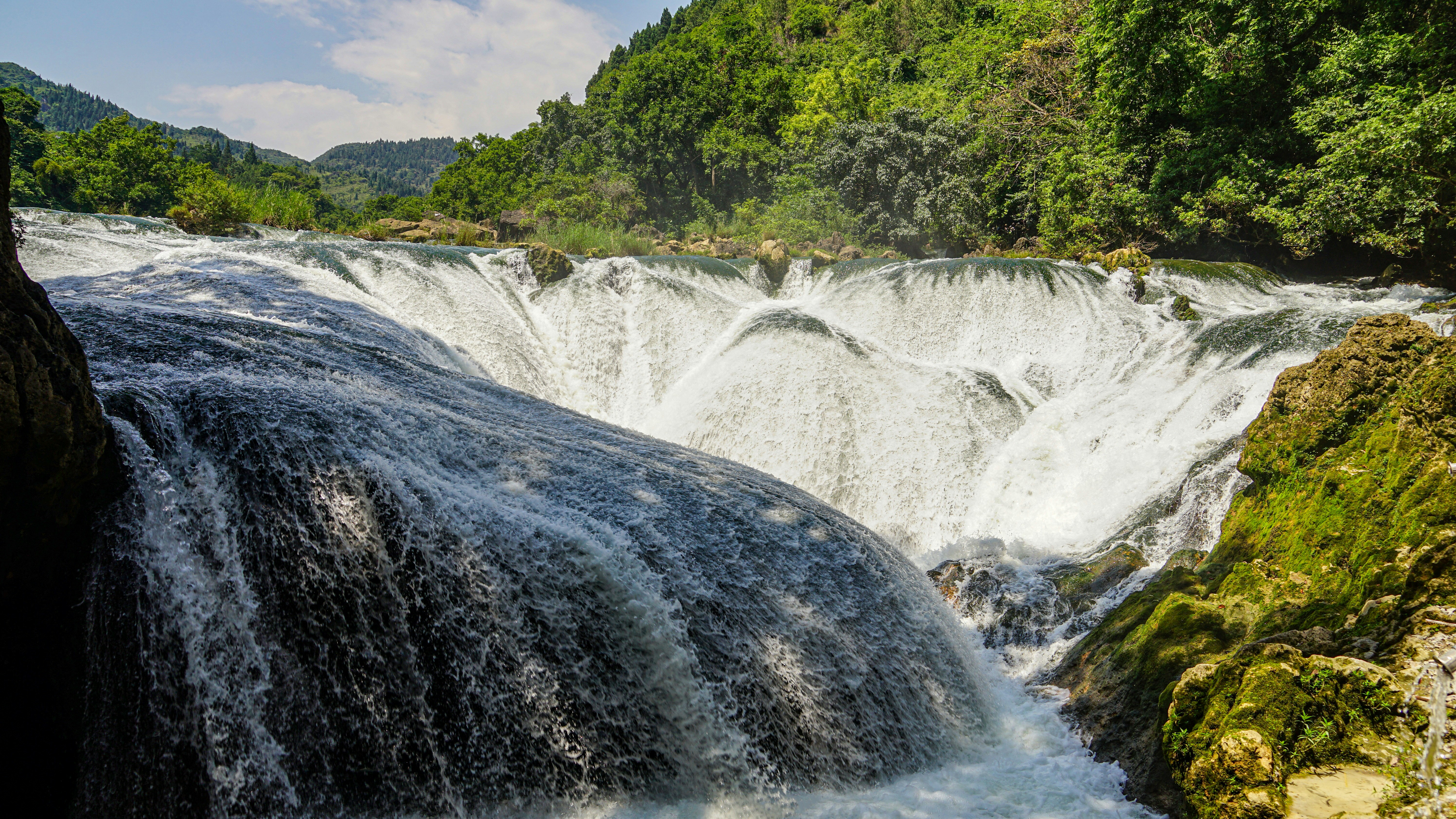 Una poderosa cascada de varios niveles atraviesa un frondoso bosque verde.