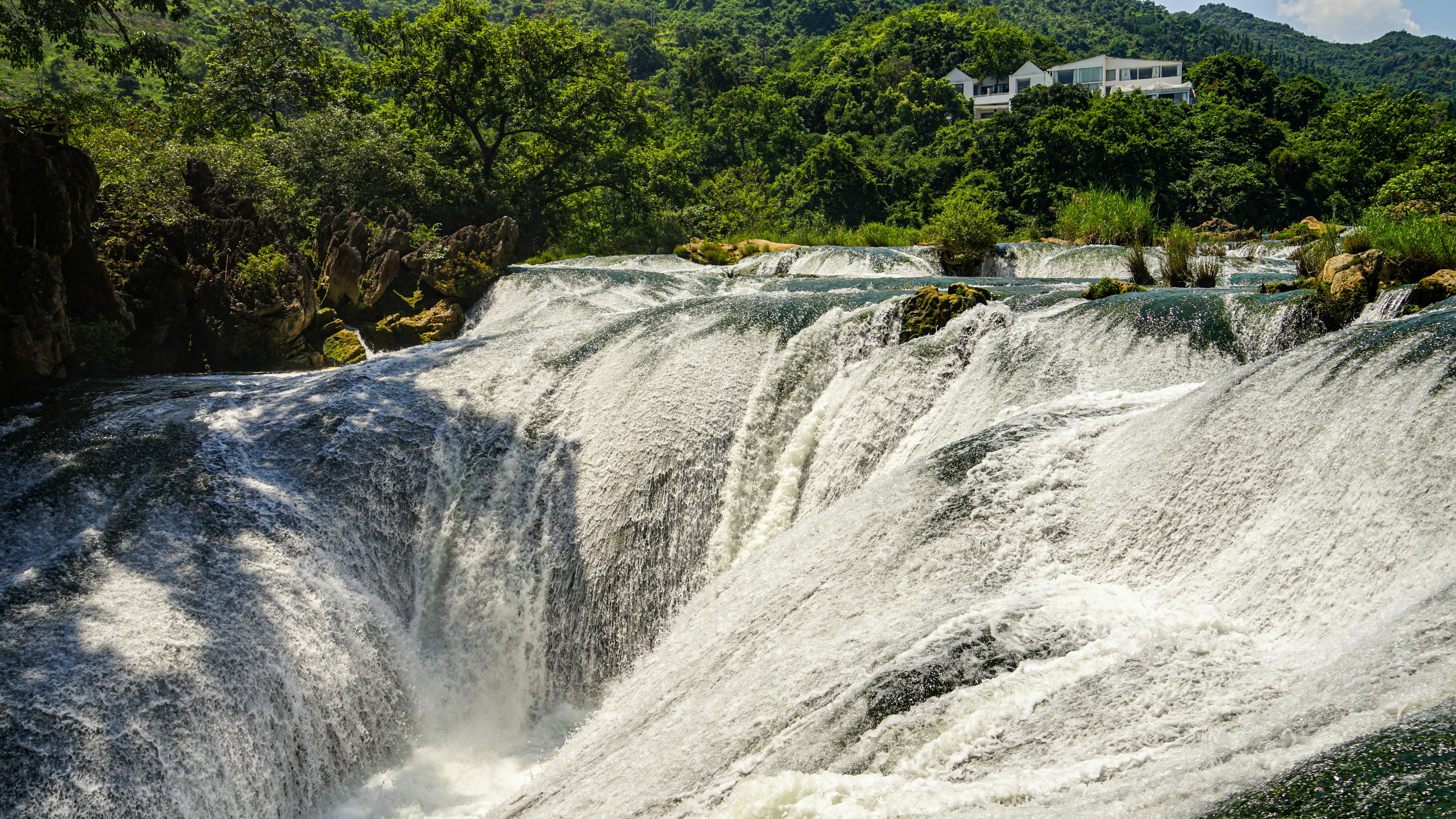 Una poderosa cascada que cae sobre las rocas con árboles verdes y frondosos.