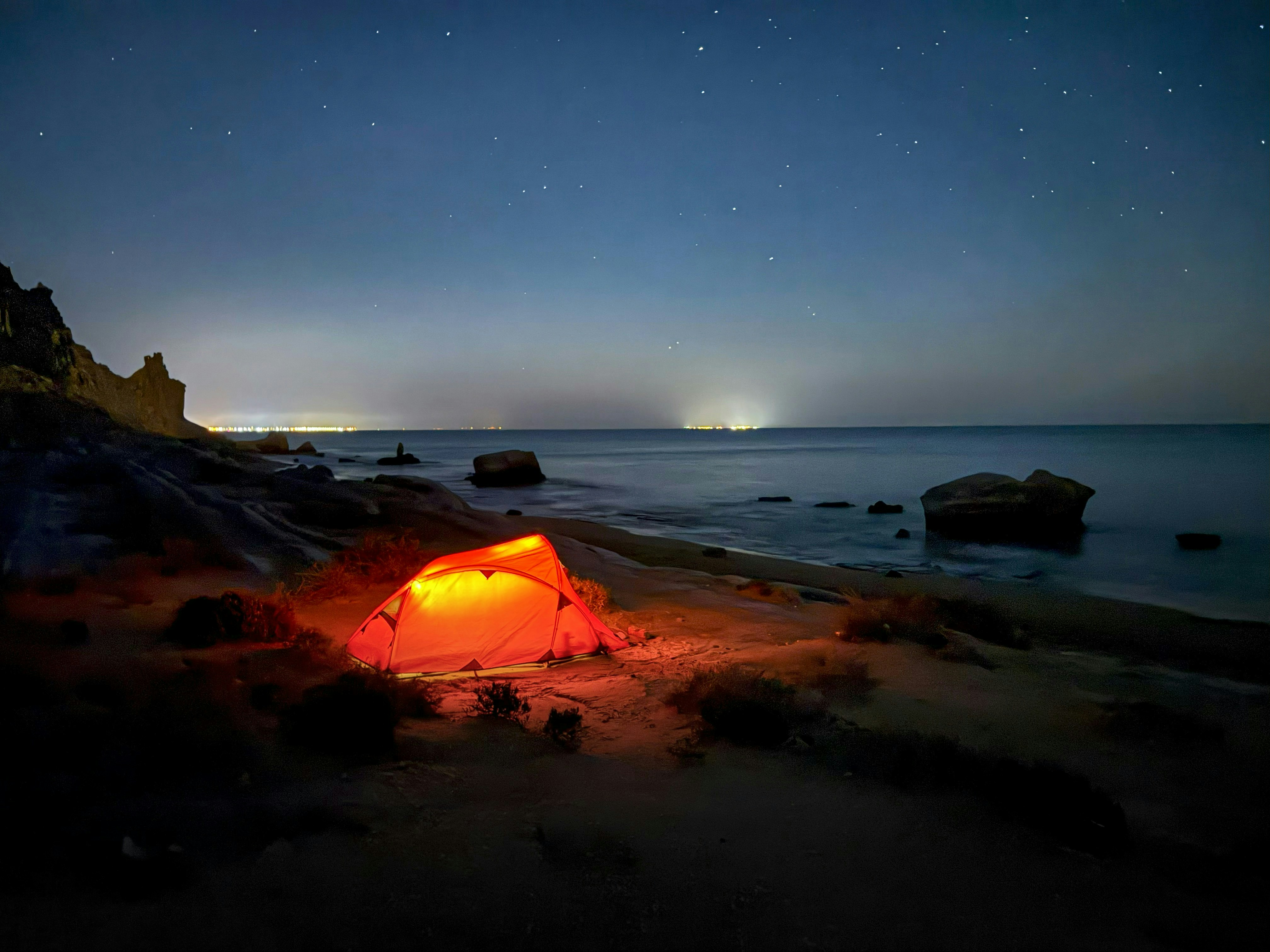 Glowing tent on a beach at night under stars