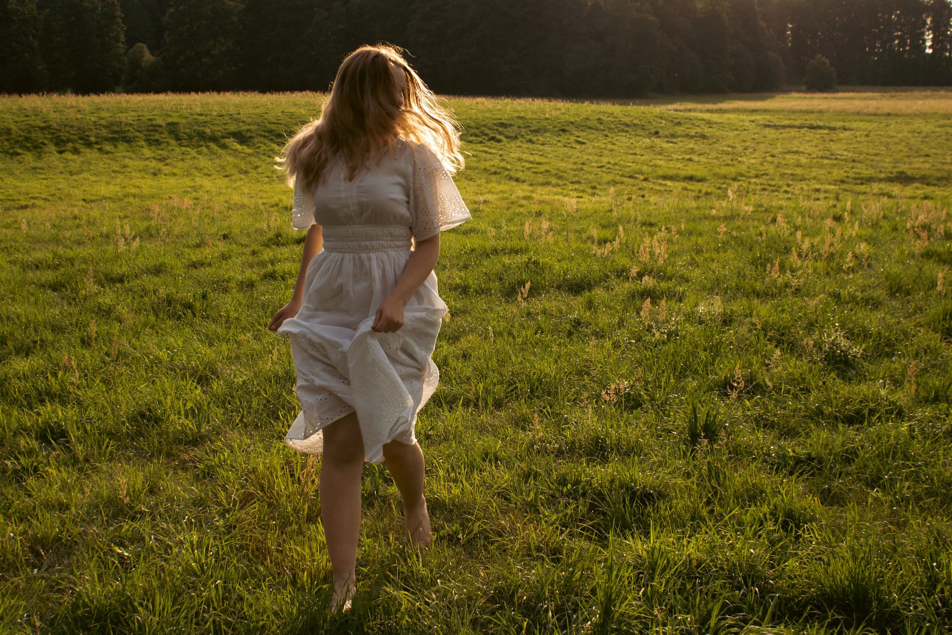 Woman running barefoot in a sunlit green field.