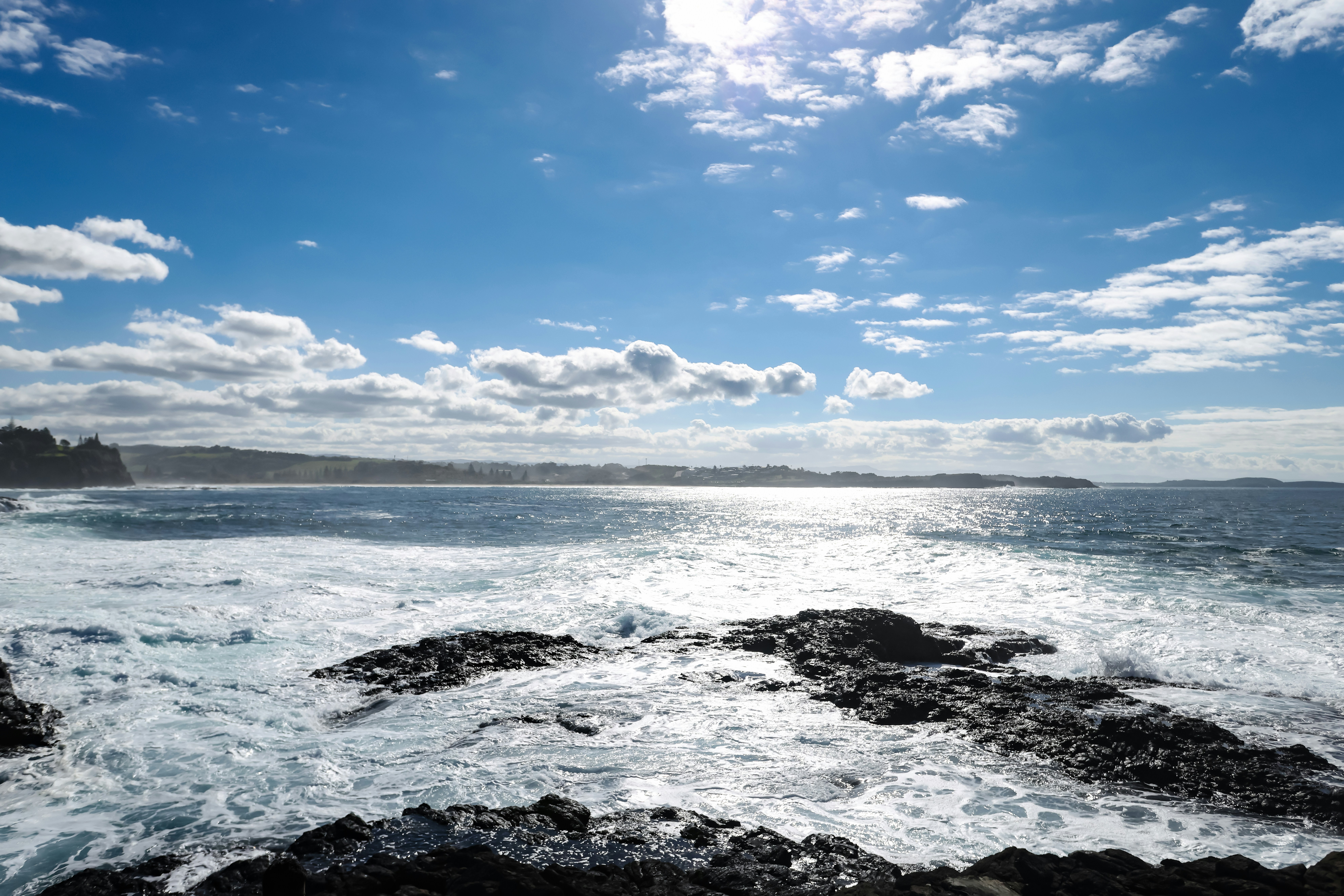 Vue ensoleillée sur l’océan avec des vagues qui déferlent sur un rivage rocheux.
