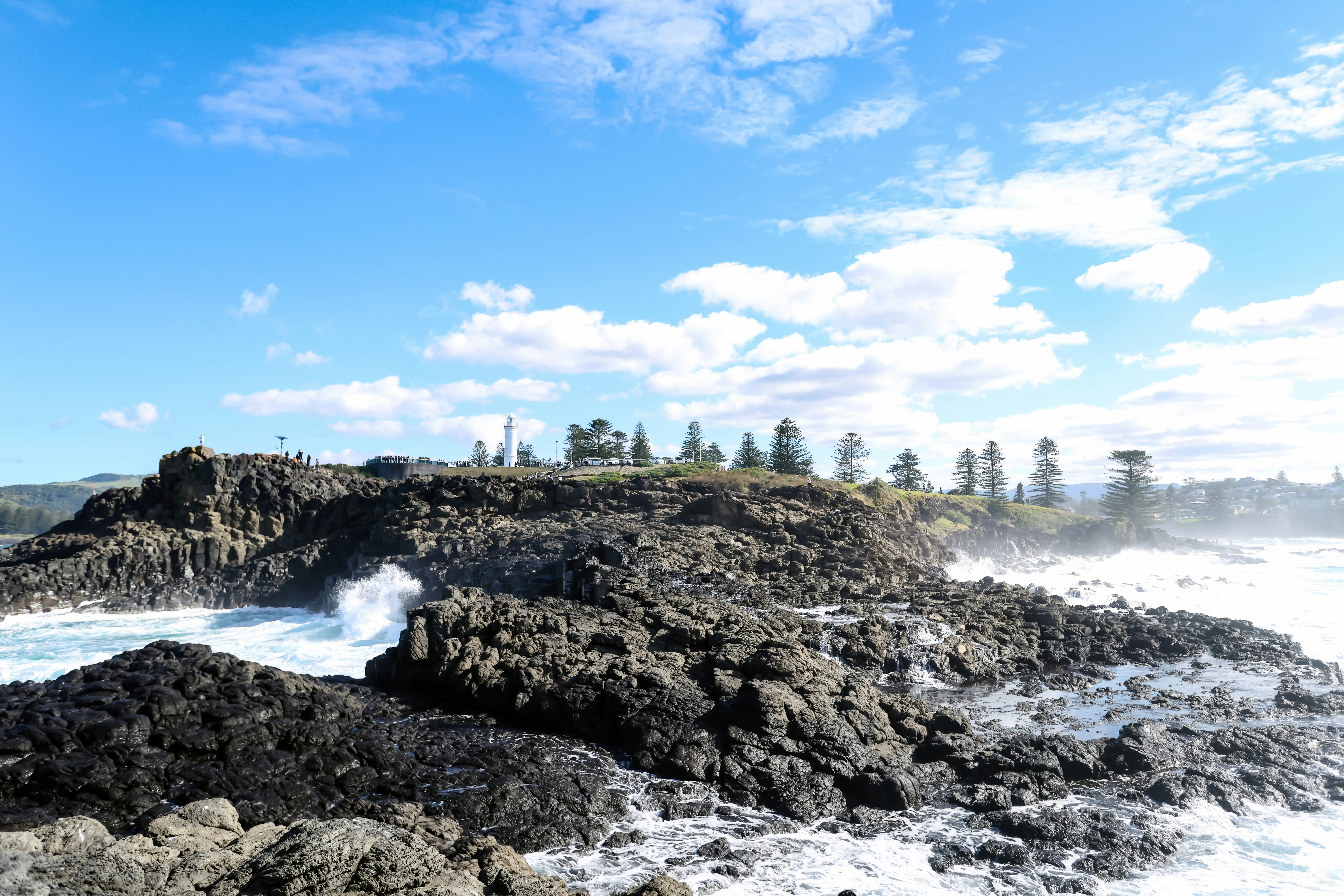 Des vagues s’écrasant sur des rochers sombres et escarpés sous un ciel bleu.
