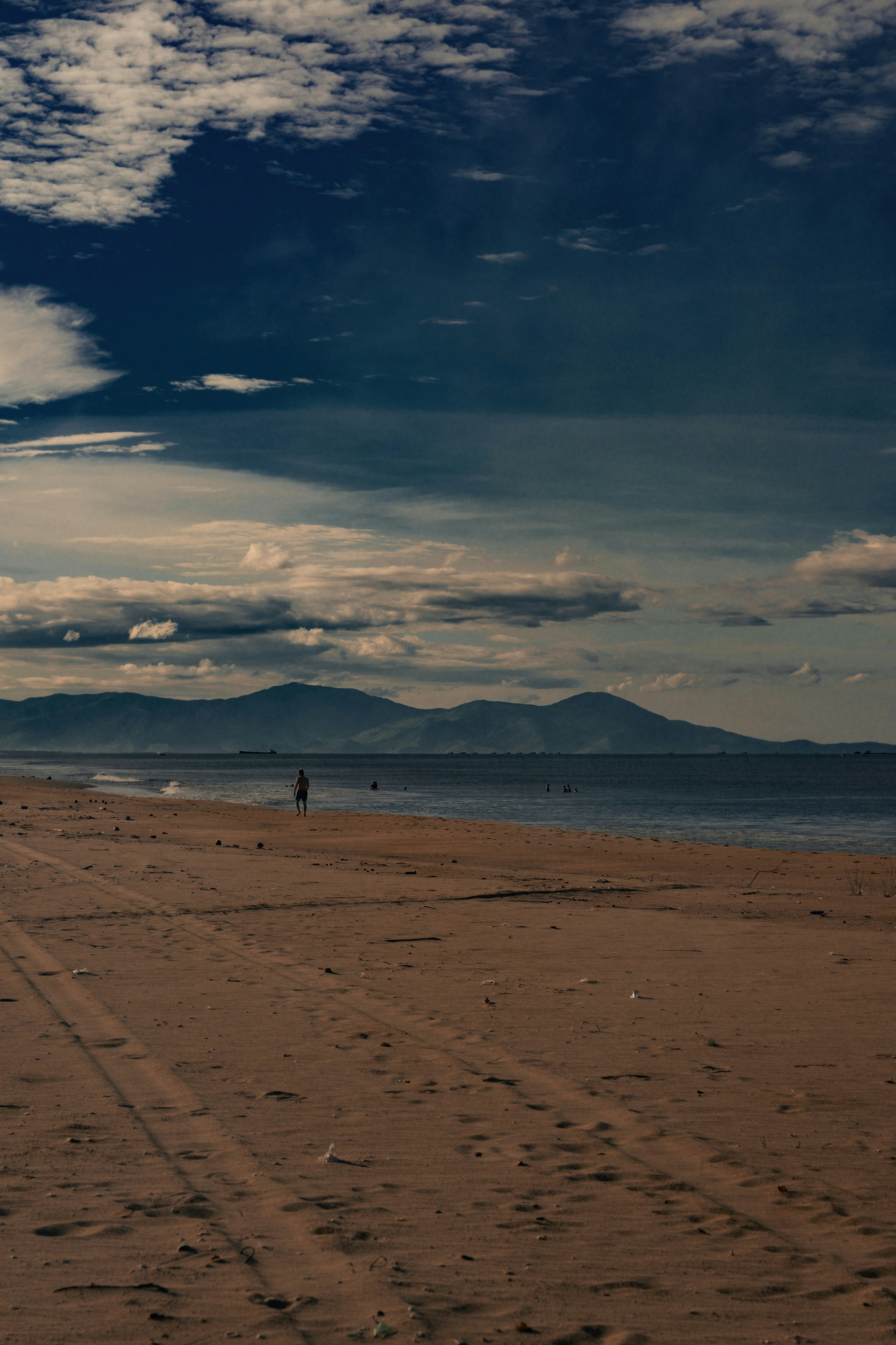 Beach with ocean, distant mountains, and dramatic cloudy sky.