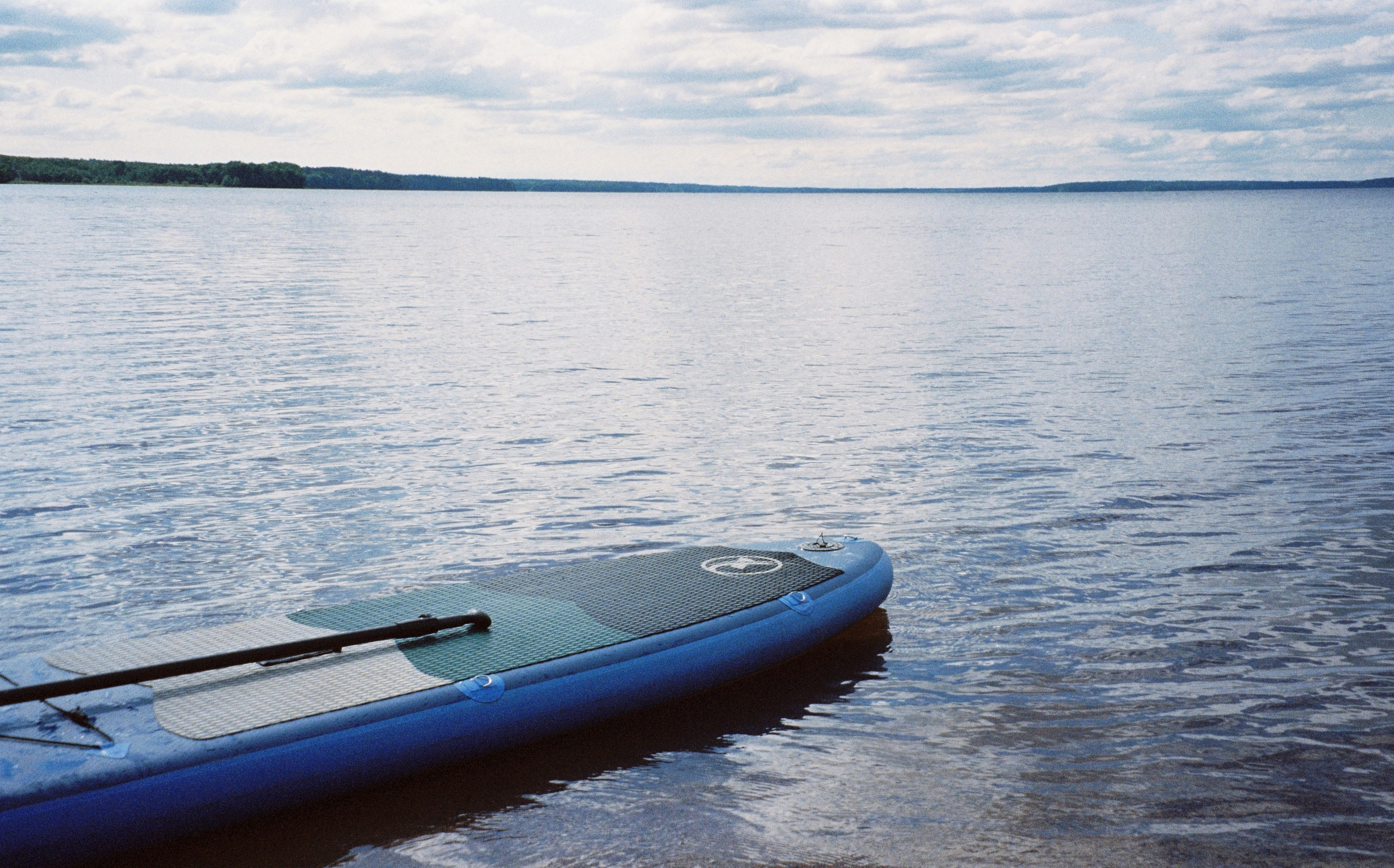 Blue paddleboard on calm lake with a cloudy sky