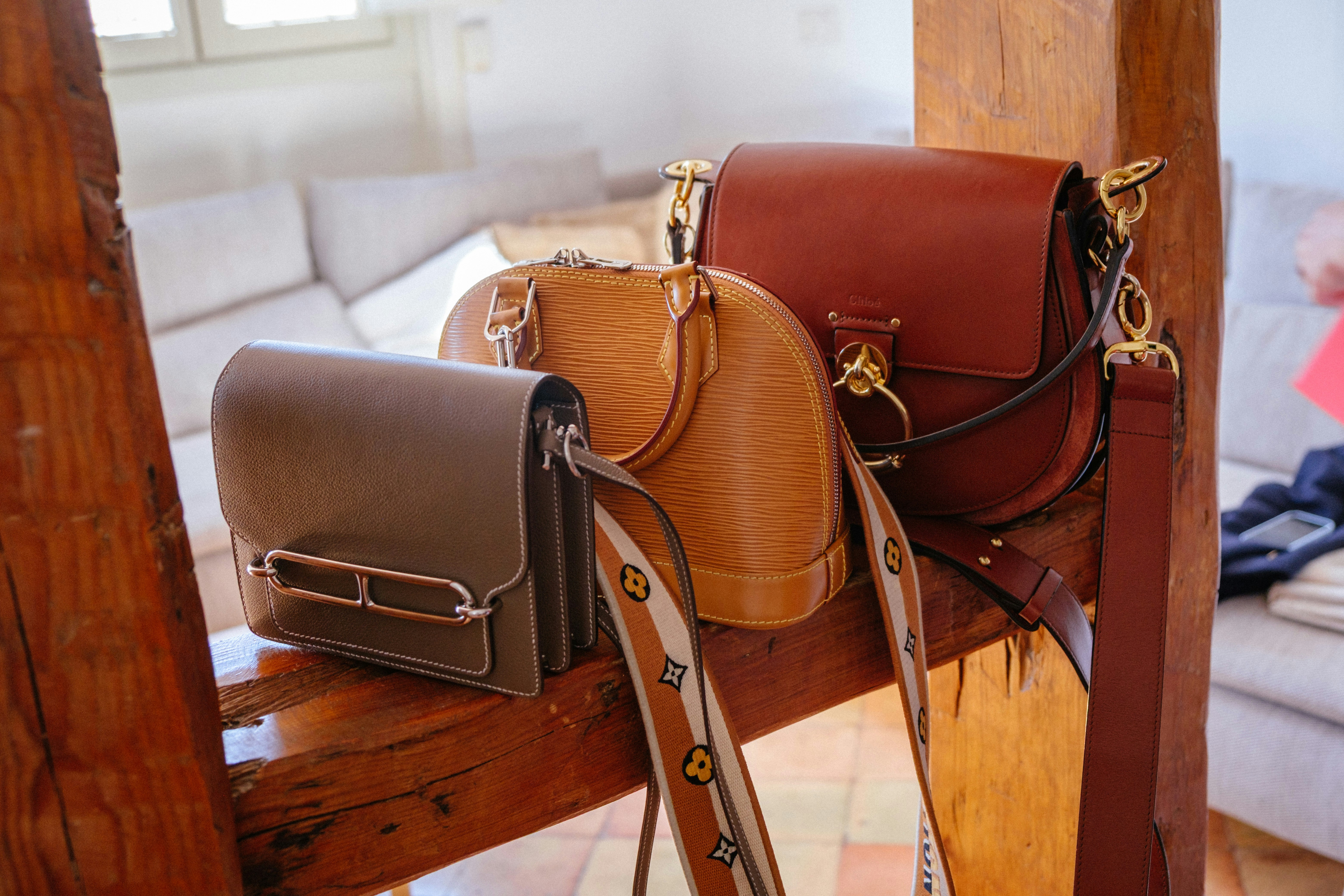 Three stylish handbags on a wooden beam