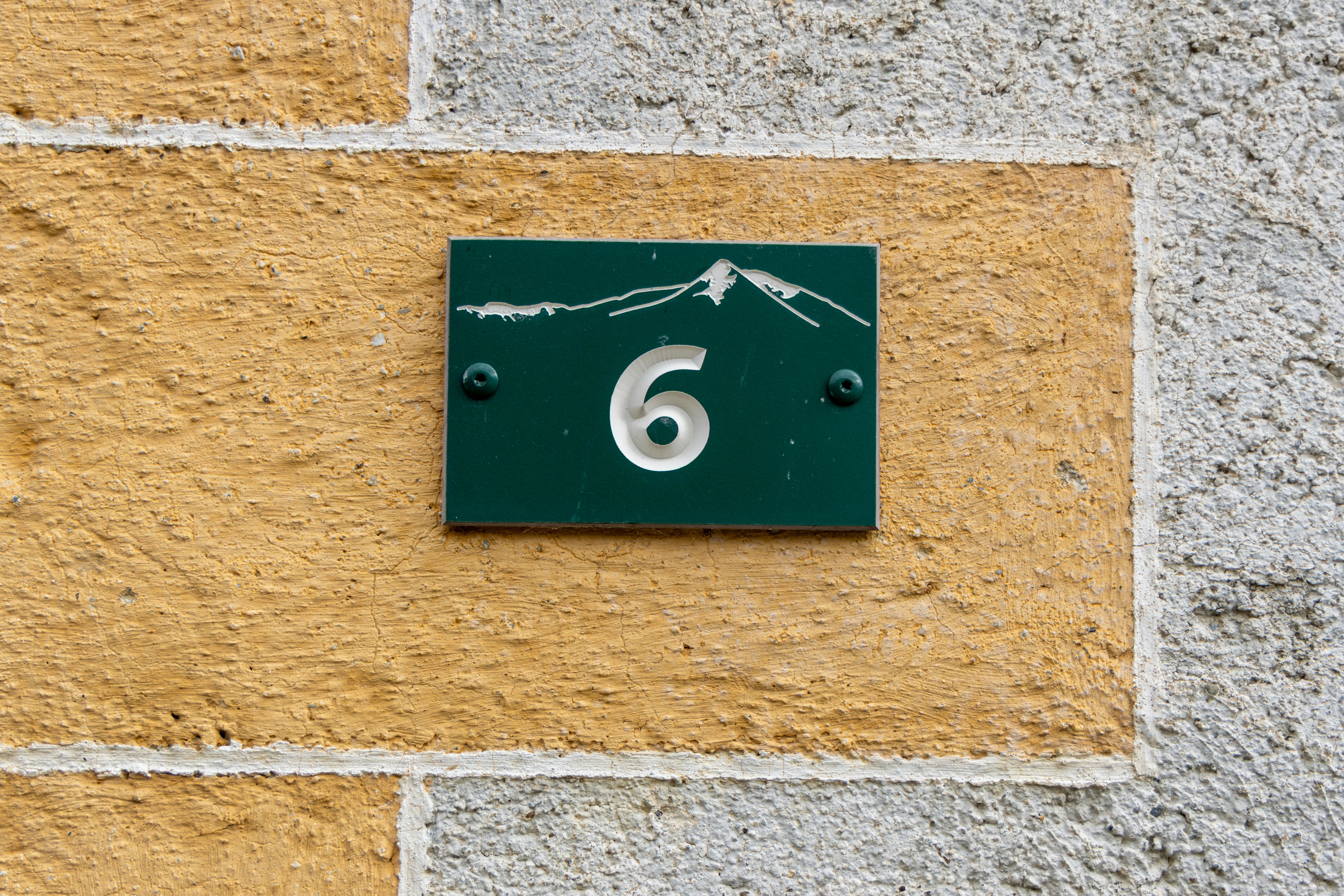 A green house number 6 plate on a stone wall