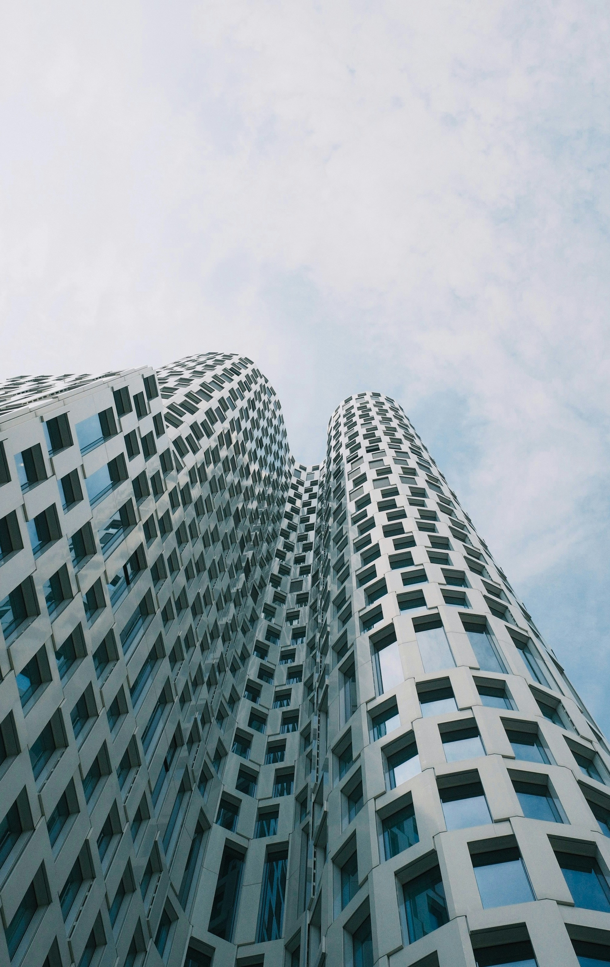 Modern wavy skyscraper with many windows against a cloudy sky