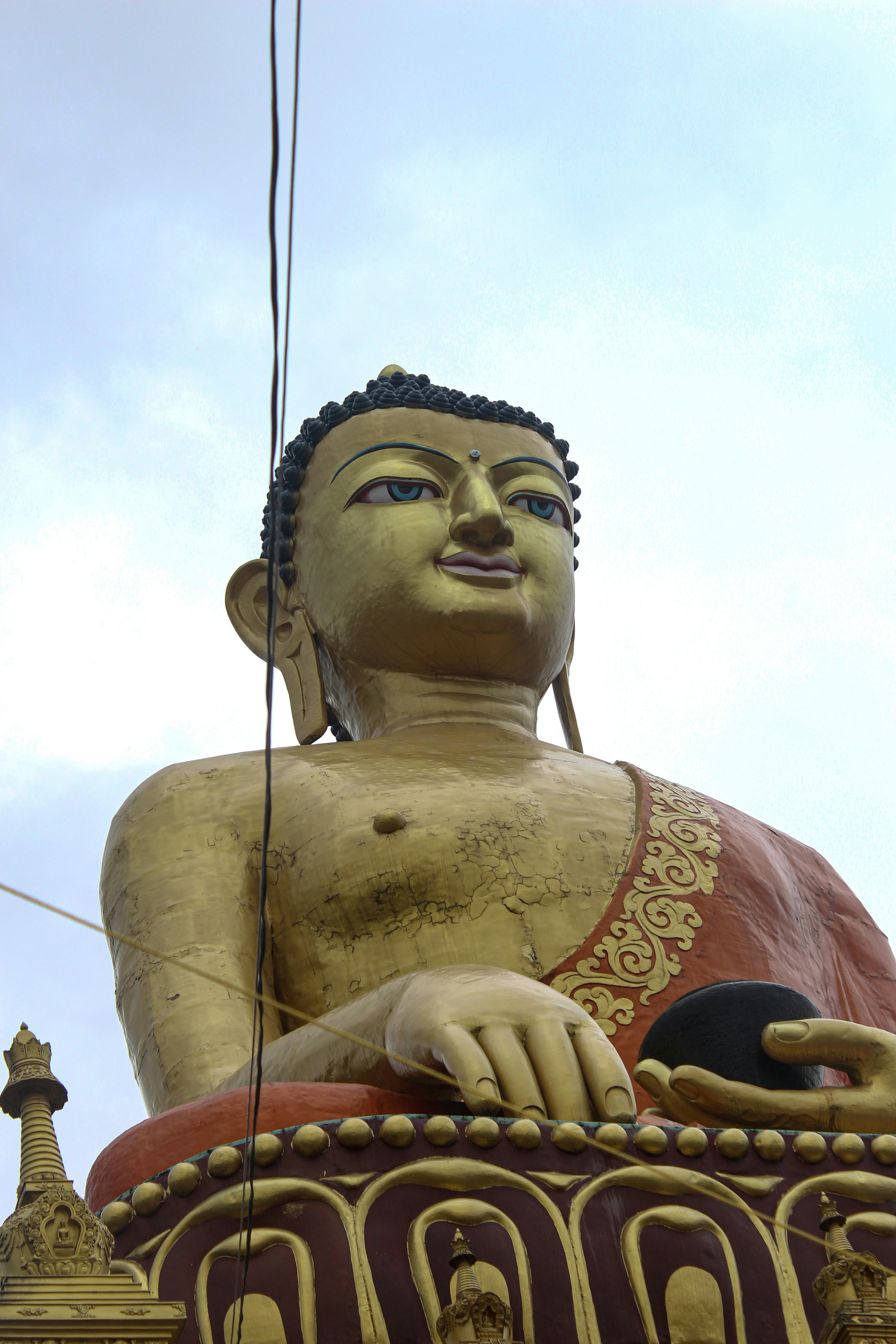 Golden buddha statue with red robe against a cloudy sky.