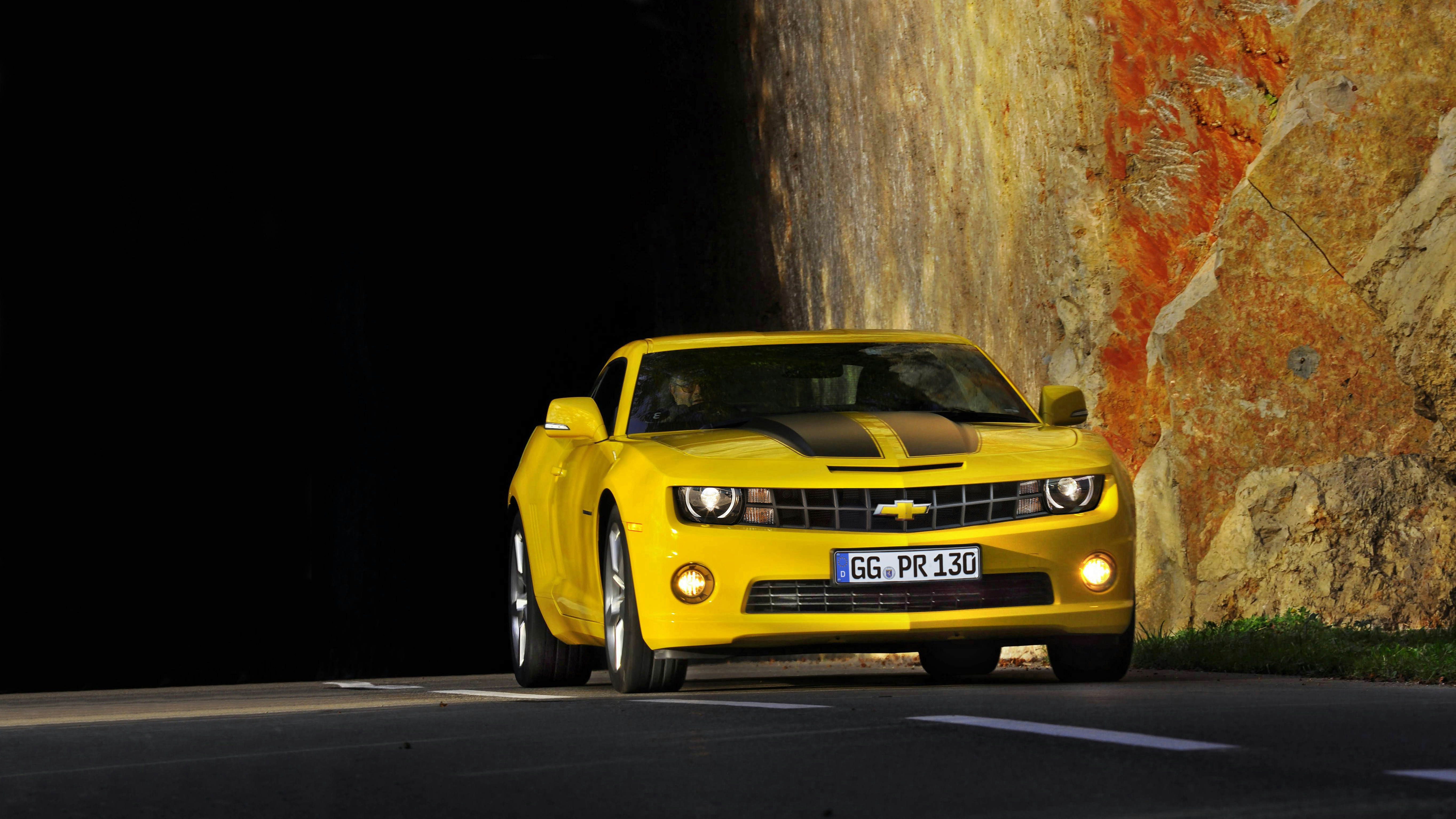 Um carro esportivo amarelo Camaro saindo de um túnel escuro.