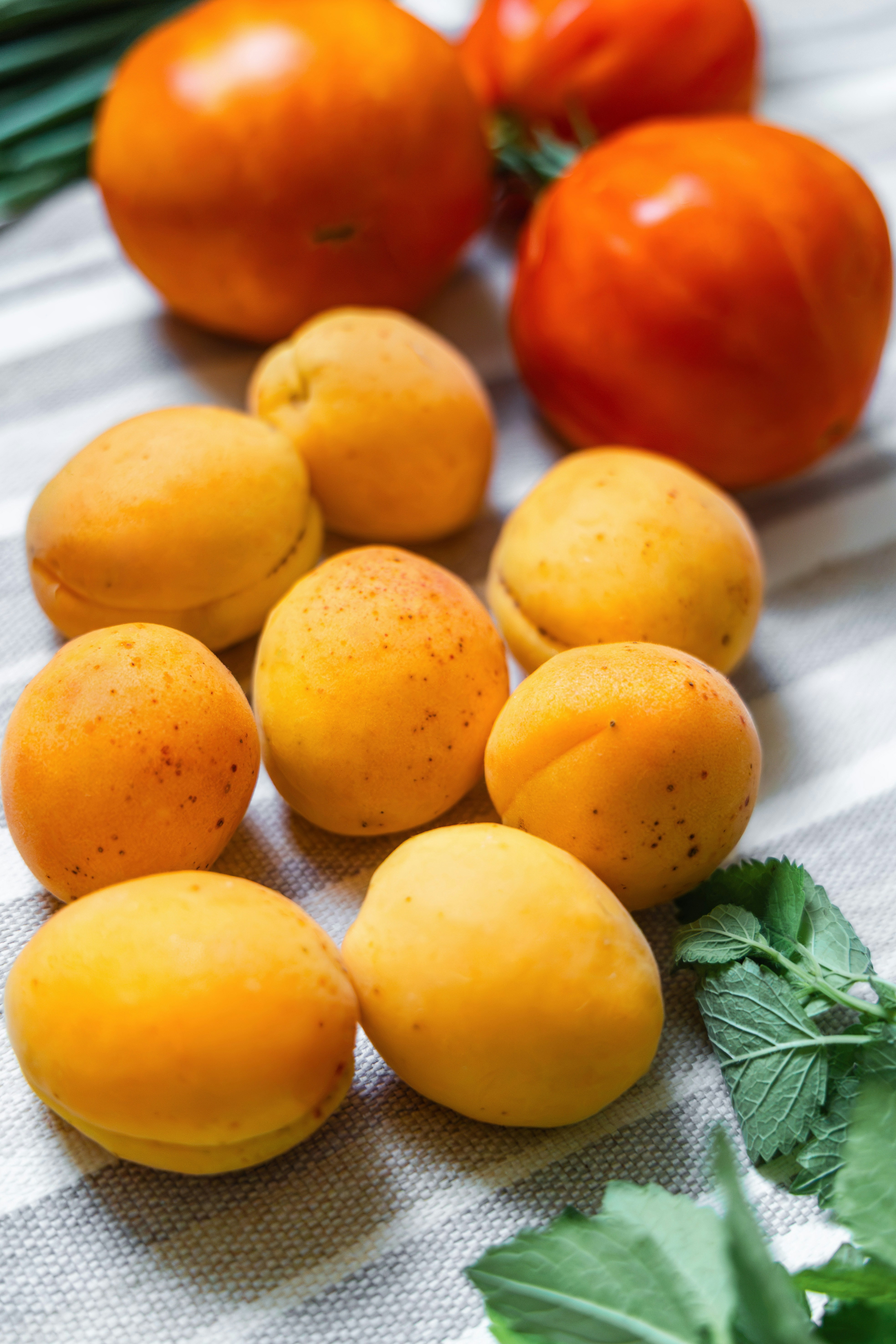 Fresh apricots, tomatoes, and mint leaves on a striped cloth.