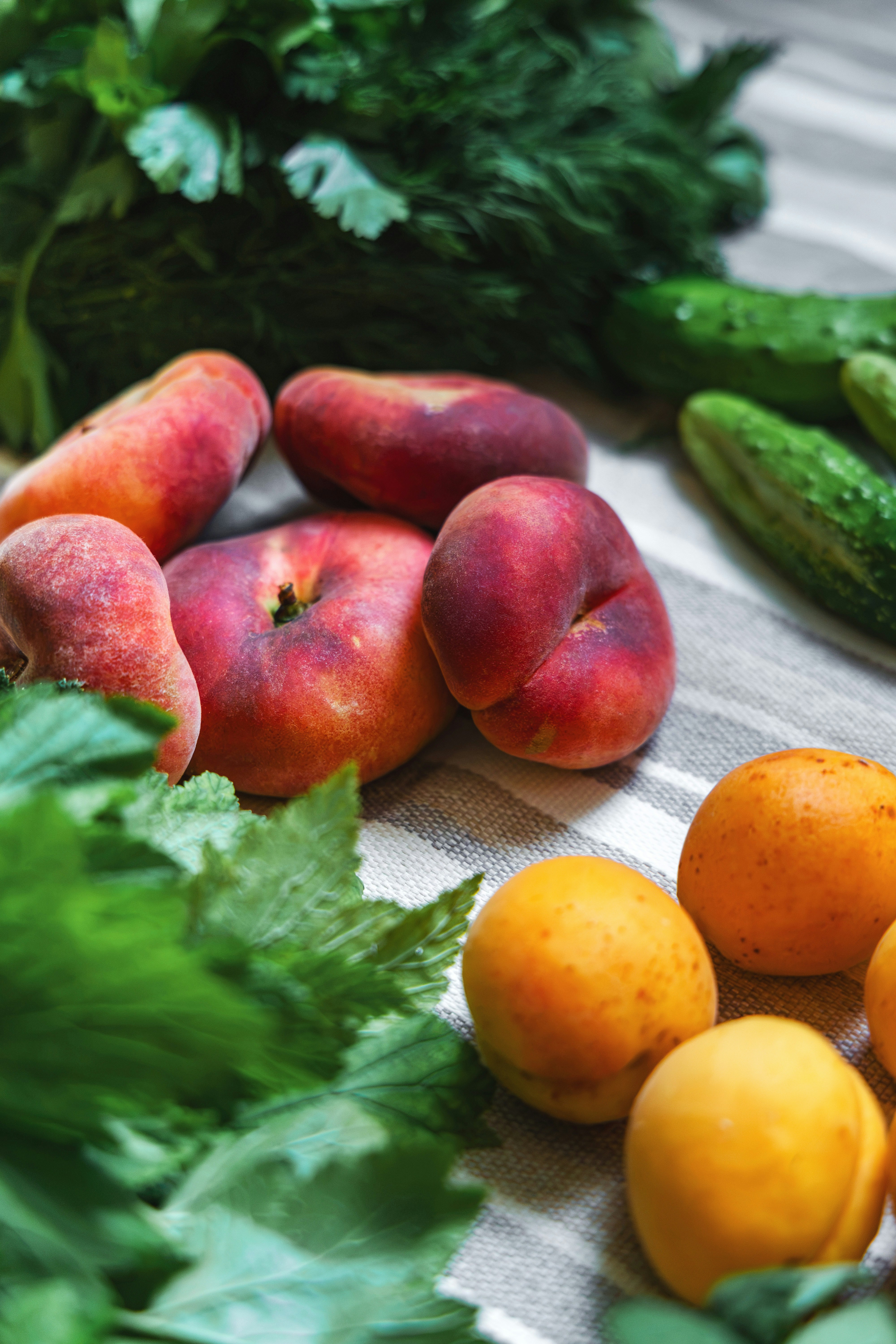 Fresh peaches, apricots, cucumbers, and greens on a striped cloth.