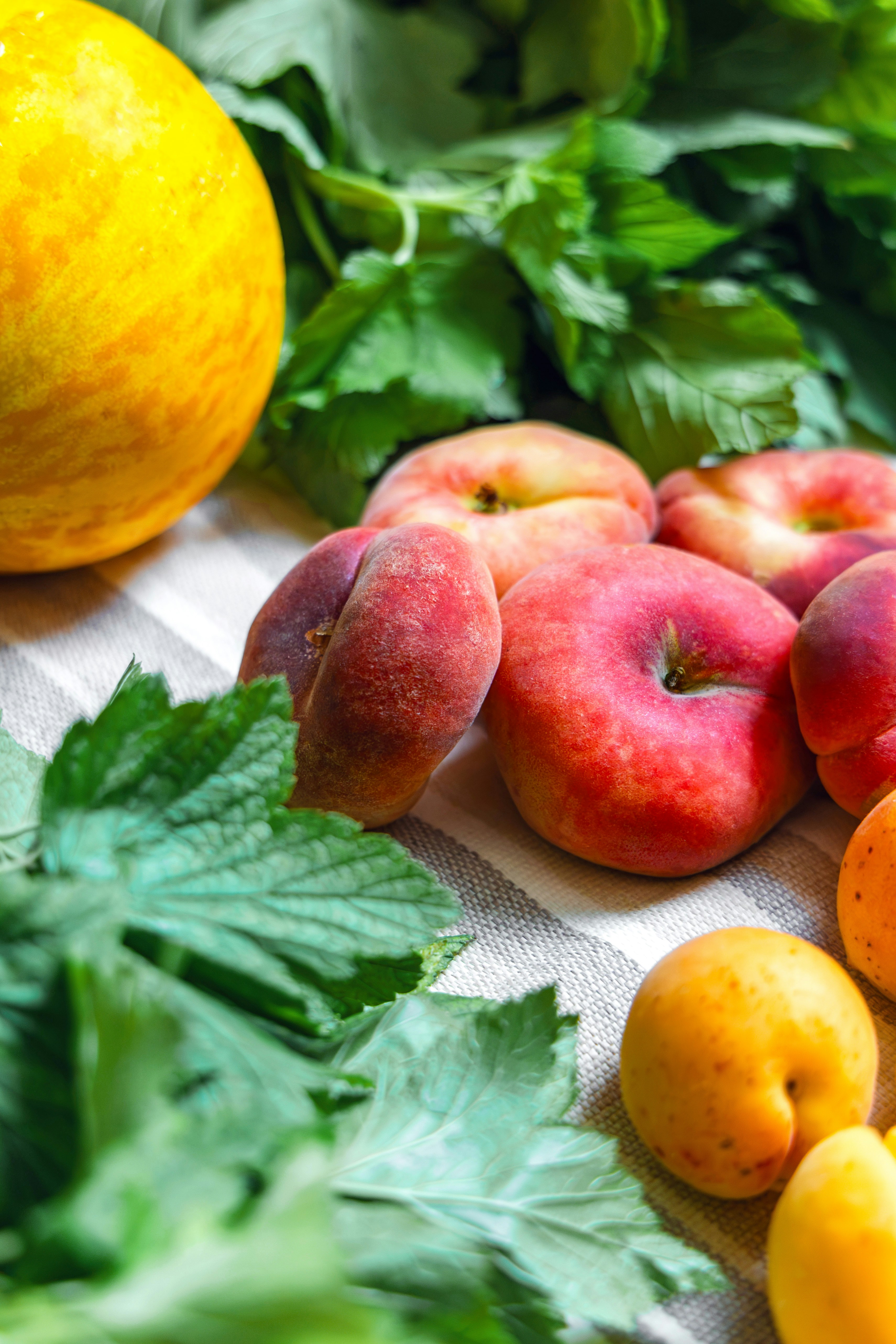 Fresh peaches, apricots, melon, and green leaves on cloth.