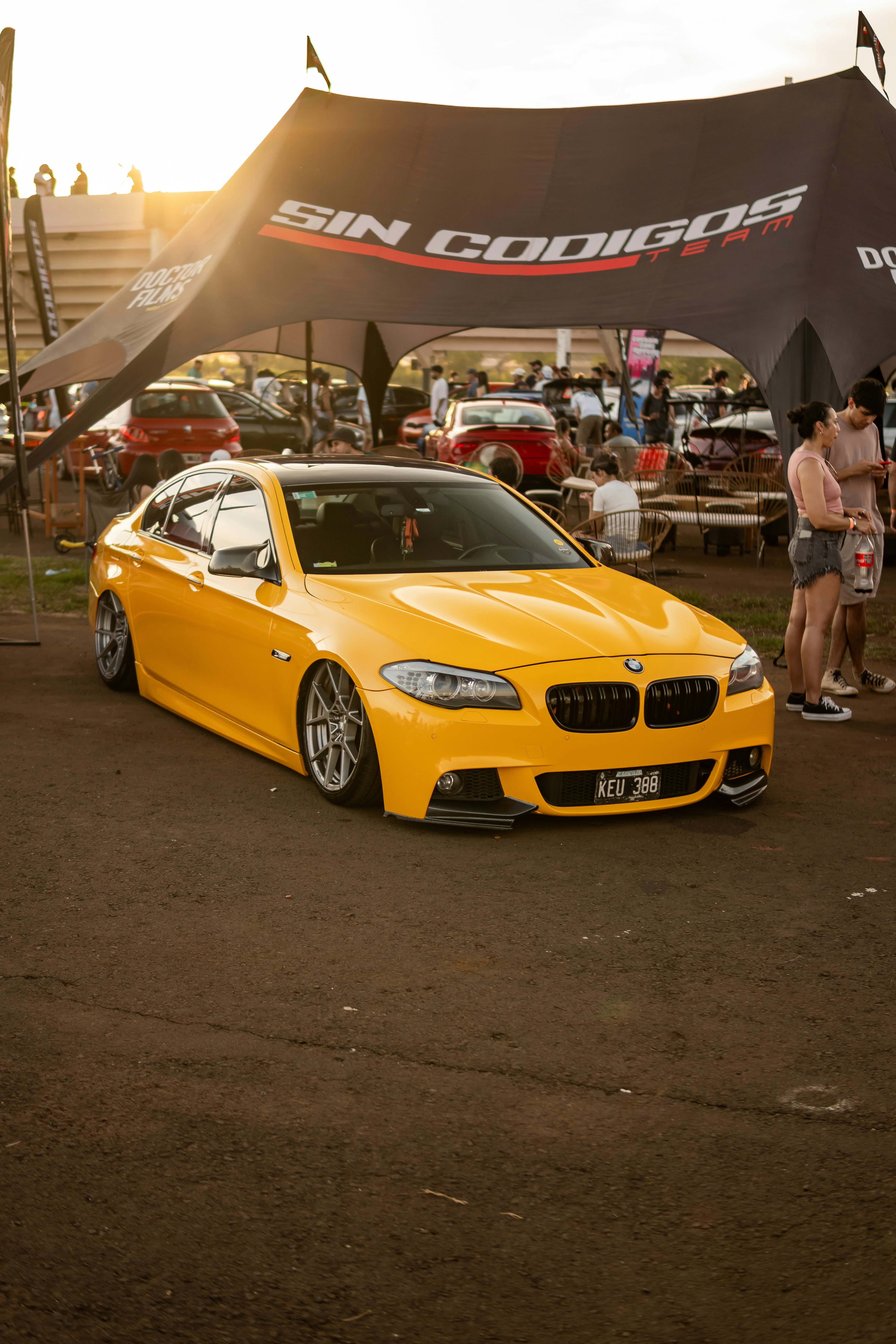 Carro BMW amarelo com rodas personalizadas em evento ao ar livre.
