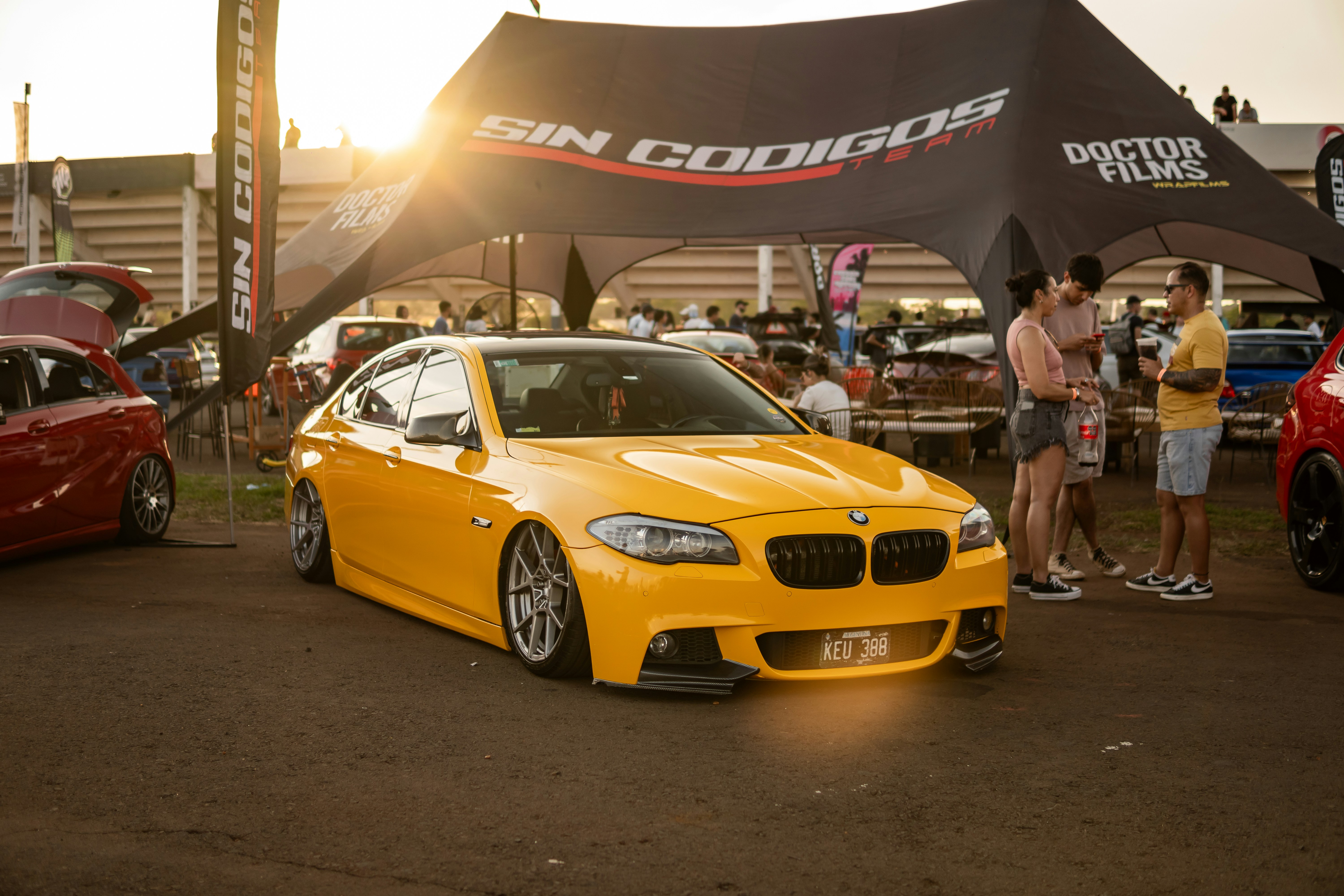 BMW amarelo modificado sob uma barraca ao pôr do sol.